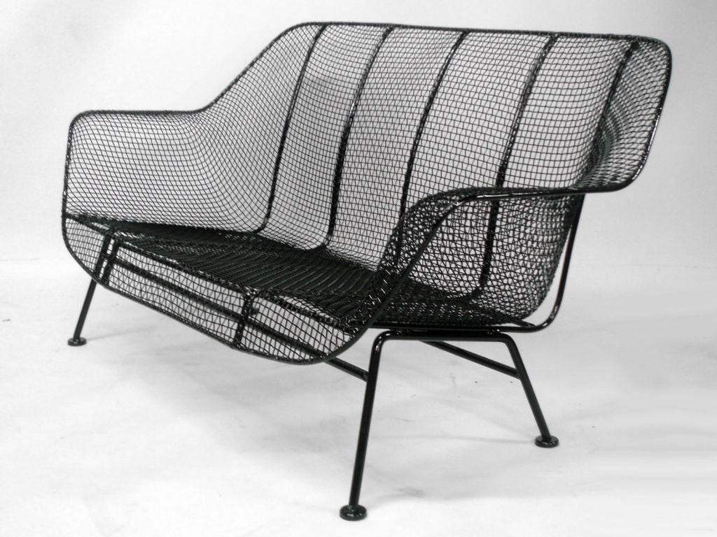 A wrought iron and mesh settee by Russell Lee Woodard Co. Properly restored in gloss black powder coat with new foot glides installed.