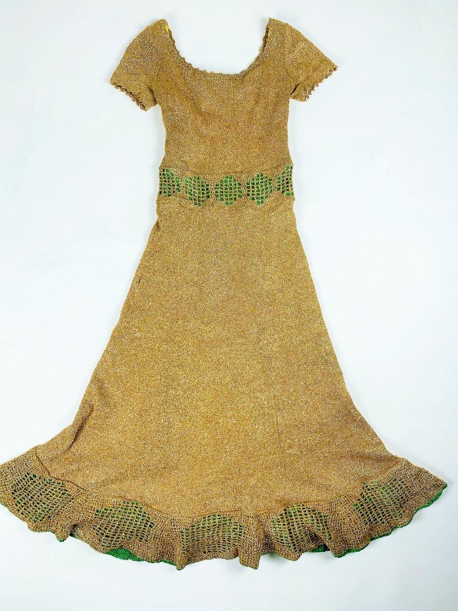 Circa 1970

France

Long party dress made of gold Lurex and green fluorescent Lurex knitwear and dating from the 1970s. Tight dress with boat neckline and short sleeves. Mesh effect in the waistband and in the bottom flounce showing the green Lurex