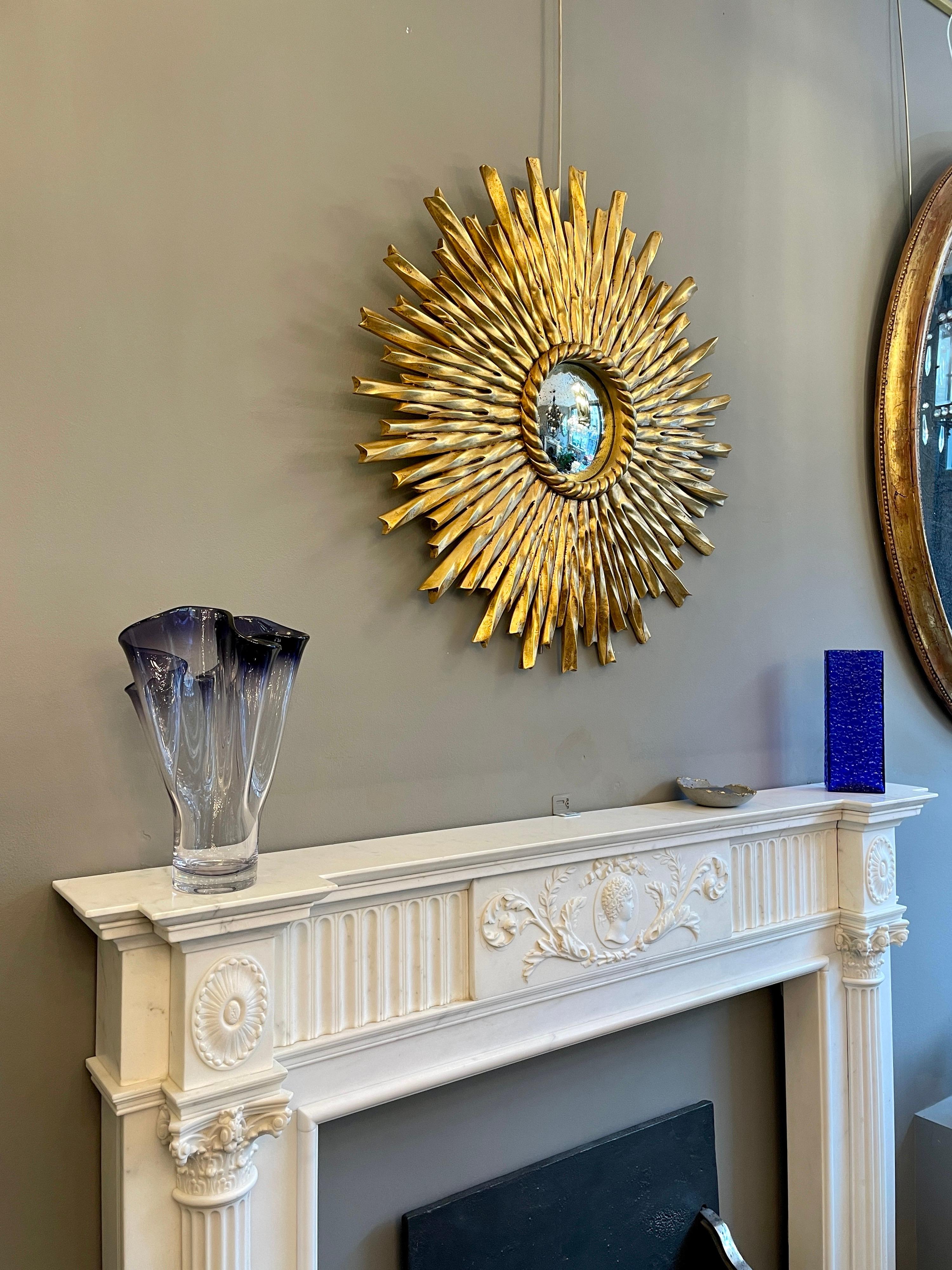 A vibrant gold gilt convex mirror with distressed glass, sitting within a rope twist border and twisted rays with edged finish. Carved from Mahogany. Contemporary.
