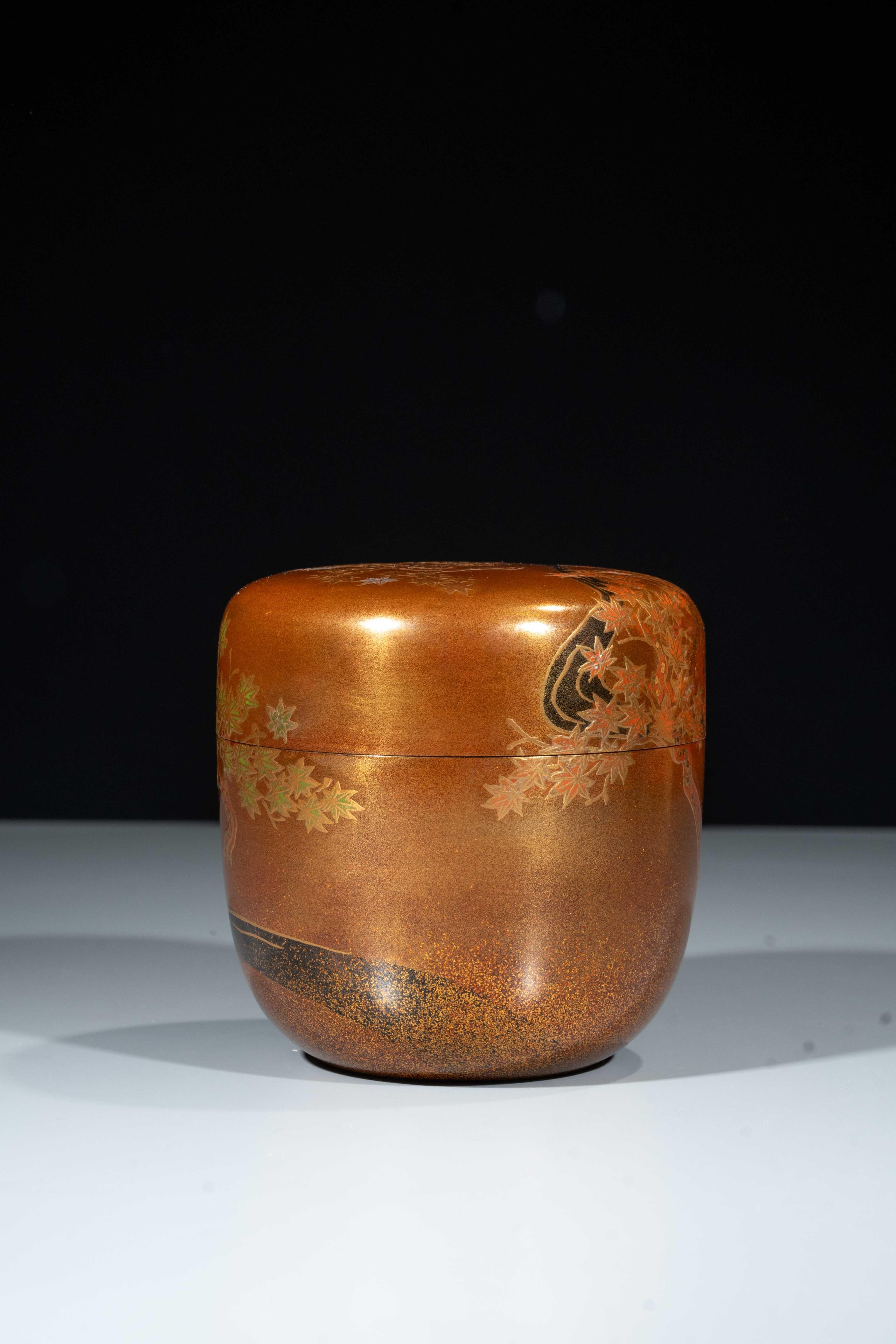 Eine Teedose (Natsume) aus Goldlack, verziert mit einem Muster aus Ahornblättern und Pflanzen (Momiji), die sich entlang eines fließenden Baches erstrecken. Auf dem Deckel streckt sich ein mit Blättern beladener Branch über das Wasser. Die