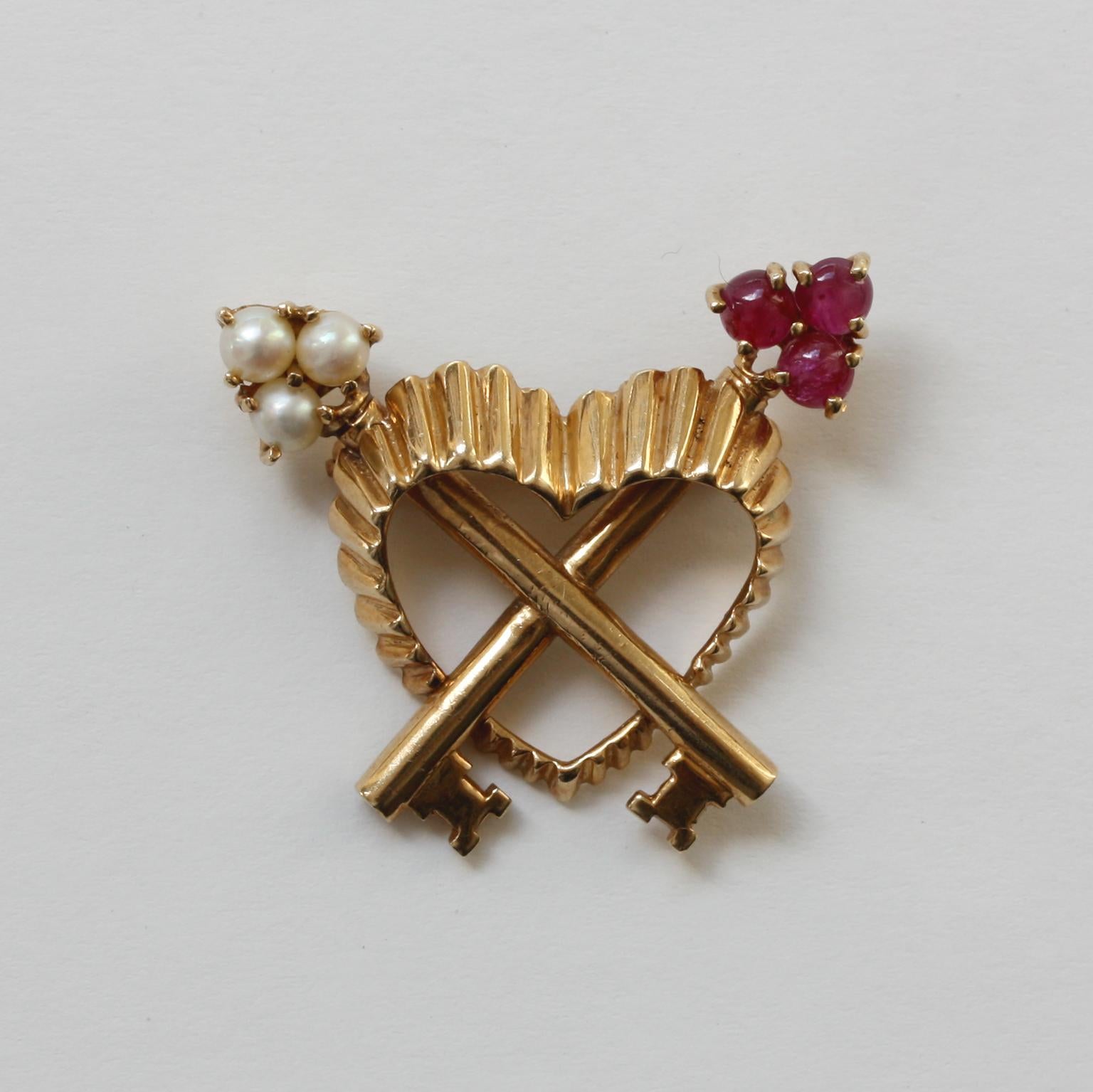 An 18 carat gold brooch in the shape of a heart with two keys across, one set with cabochon cut rubies and the other with half pearls, France, circa 1960 (this brooch can also be made into a pendant eaily).

weight: 7.70 grams
dimensions: 3.3 x 2.9