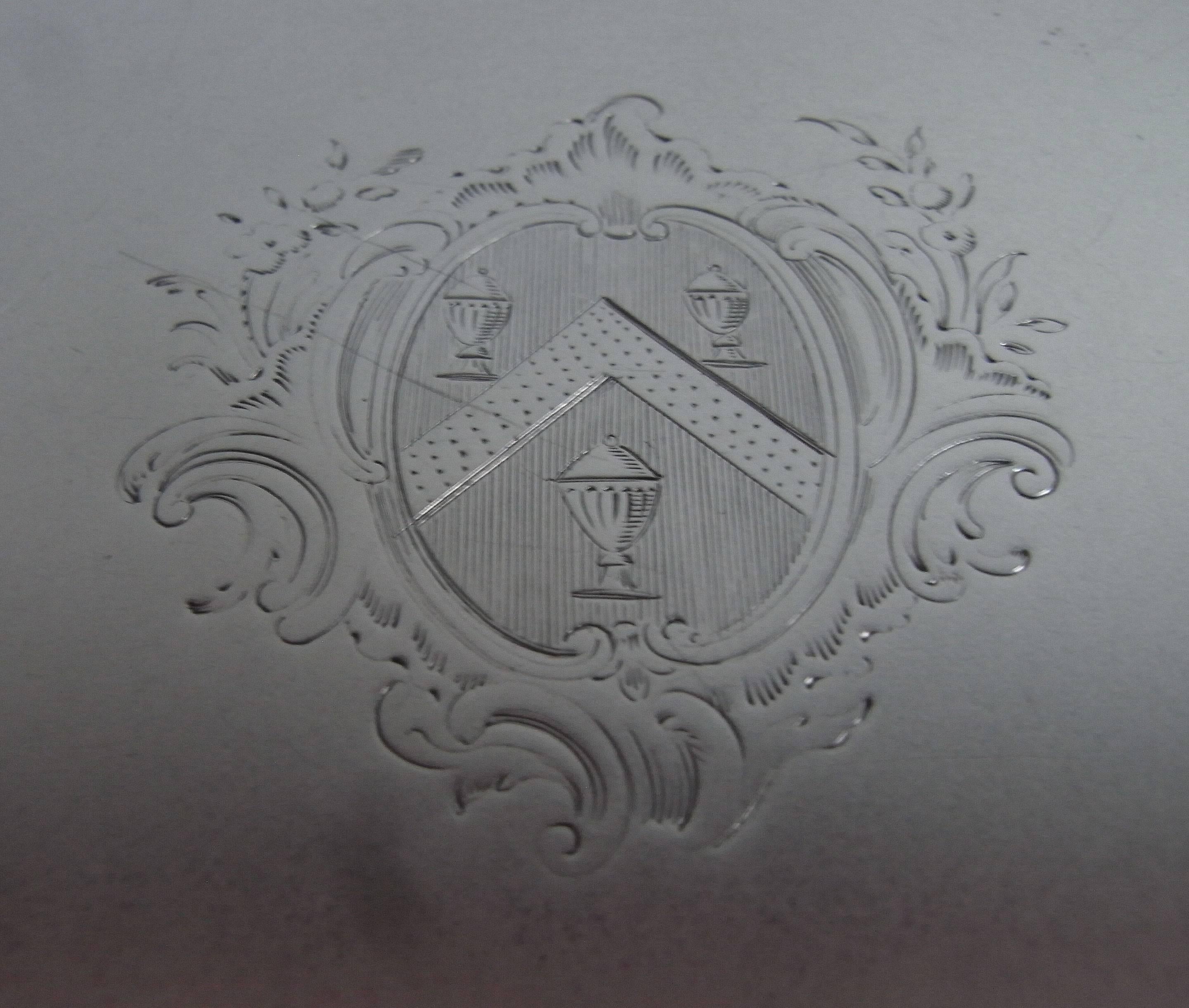 Le Salver repose sur trois pieds sabots et présente une bordure en relief décorée de volutes et de détails de coquilles rococo. Le centre du Salver est gravé d'un Armorial contemporain entouré d'un cartouche à volutes, coquilles et rinceaux. Les