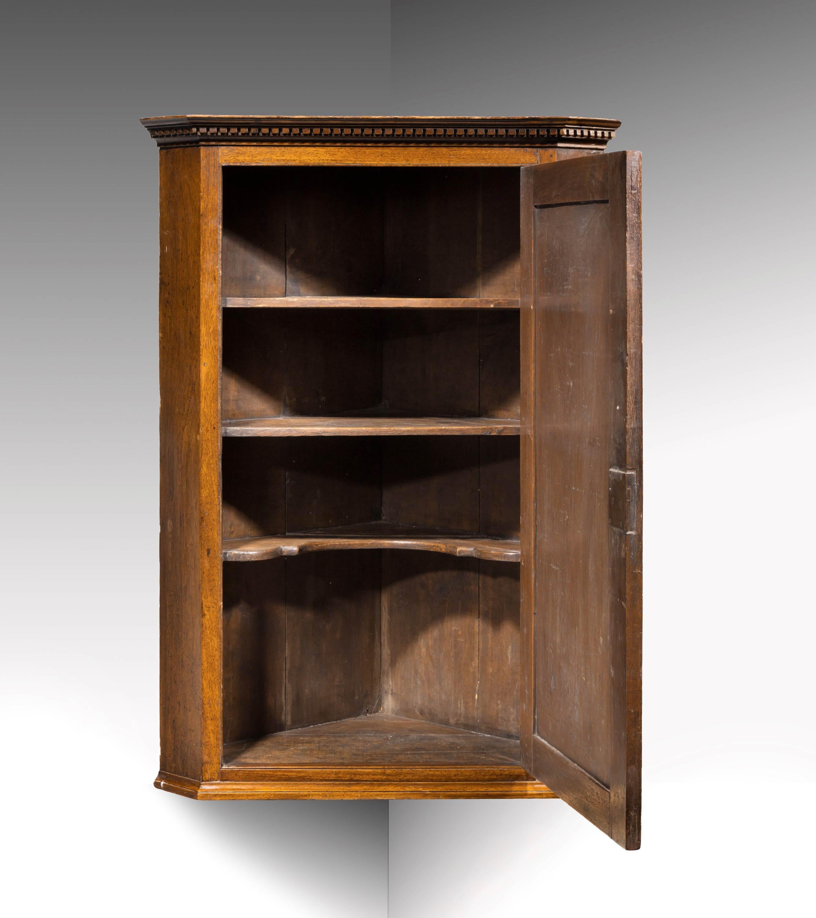 A George III period mahogany corner cupboard. A well-figured door in a recessed frame. The top with a well carved dentil cornice.
         