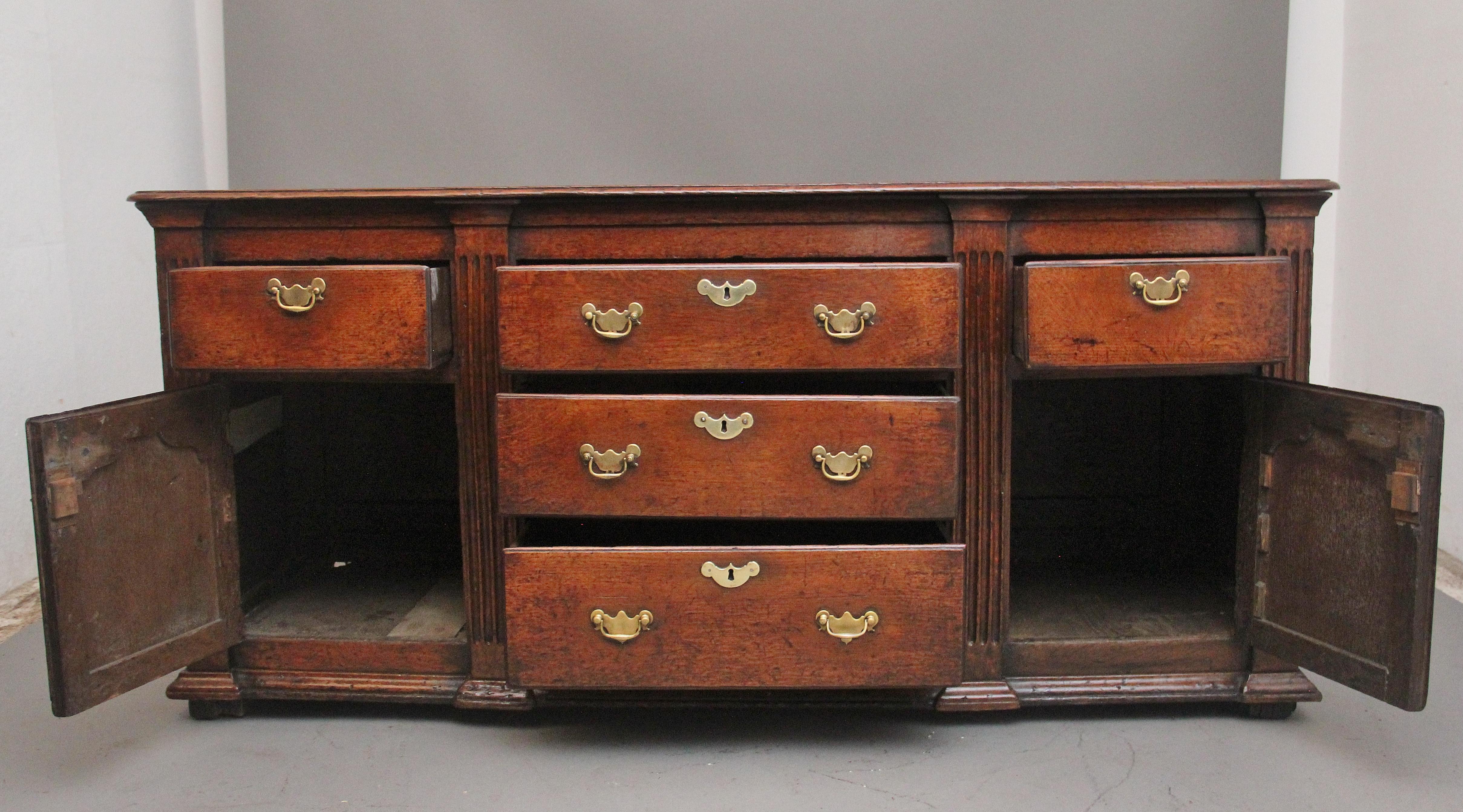 18th Century oak dresser having a nice figured and moulded edge top above three central graduated oak lined drawers flanked either side by single drawer and a cupboard below,  hinged door with arched fielded panelled door fronts, opening to reveal a