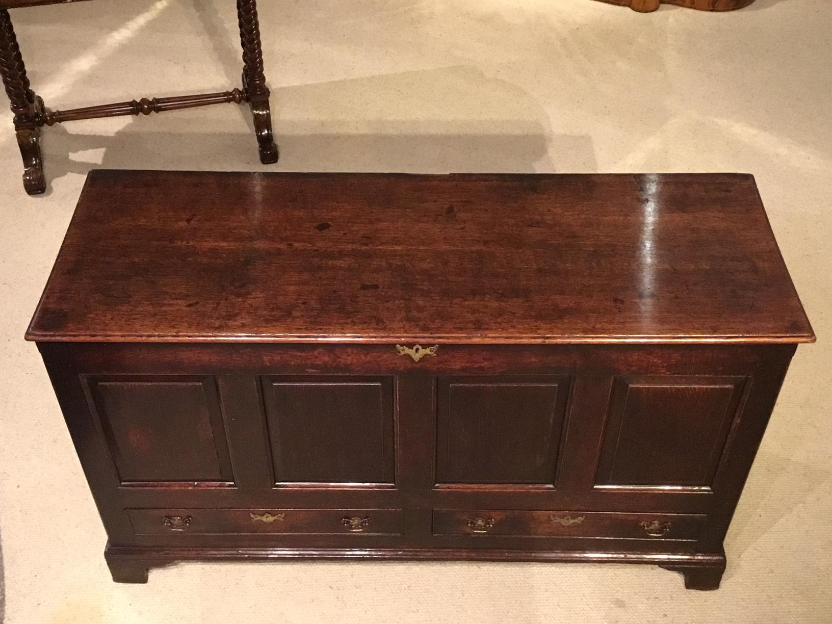 A good oak George III Period four-panel mule chest. The rectangular hinged two plank top opening to reveal ample storage. The front with four fielded panels and two oak lined rectangular drawers with brass swan neck handles and escutcheons. Standing