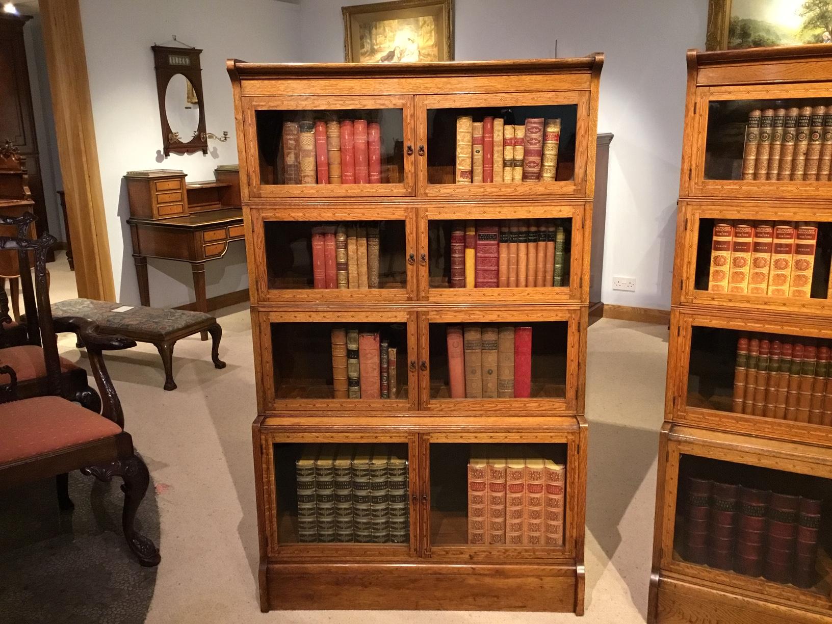 A good pair of oak sectional bookcases by William Baker & Co of Oxford. Each with a moulded top above eight hinged and glazed doors with fine tunbridge ware inlaid detail and patinated brass handles. Supported on a solid oak plinth base with solid