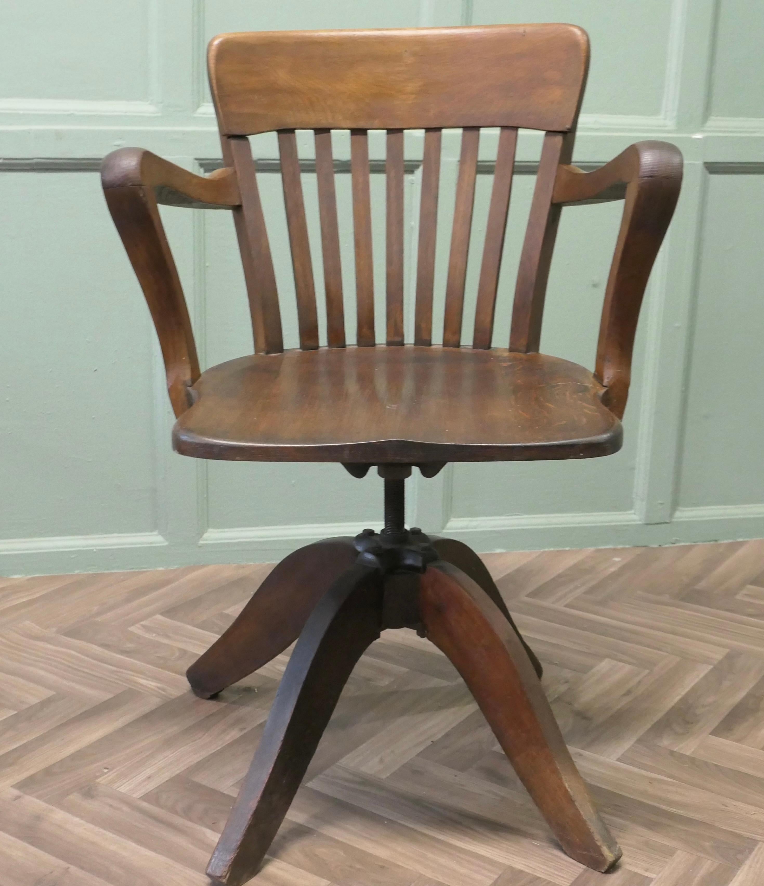 A Good Quality Art Deco Desk Chair
The Chair has an attractive deep curving back top rail with slats and arching Shepherds Crook Arm Rests. The Chair has a sculptured seat and revolves, also the height can be adjusted from 17” to 19.5”
The back of
