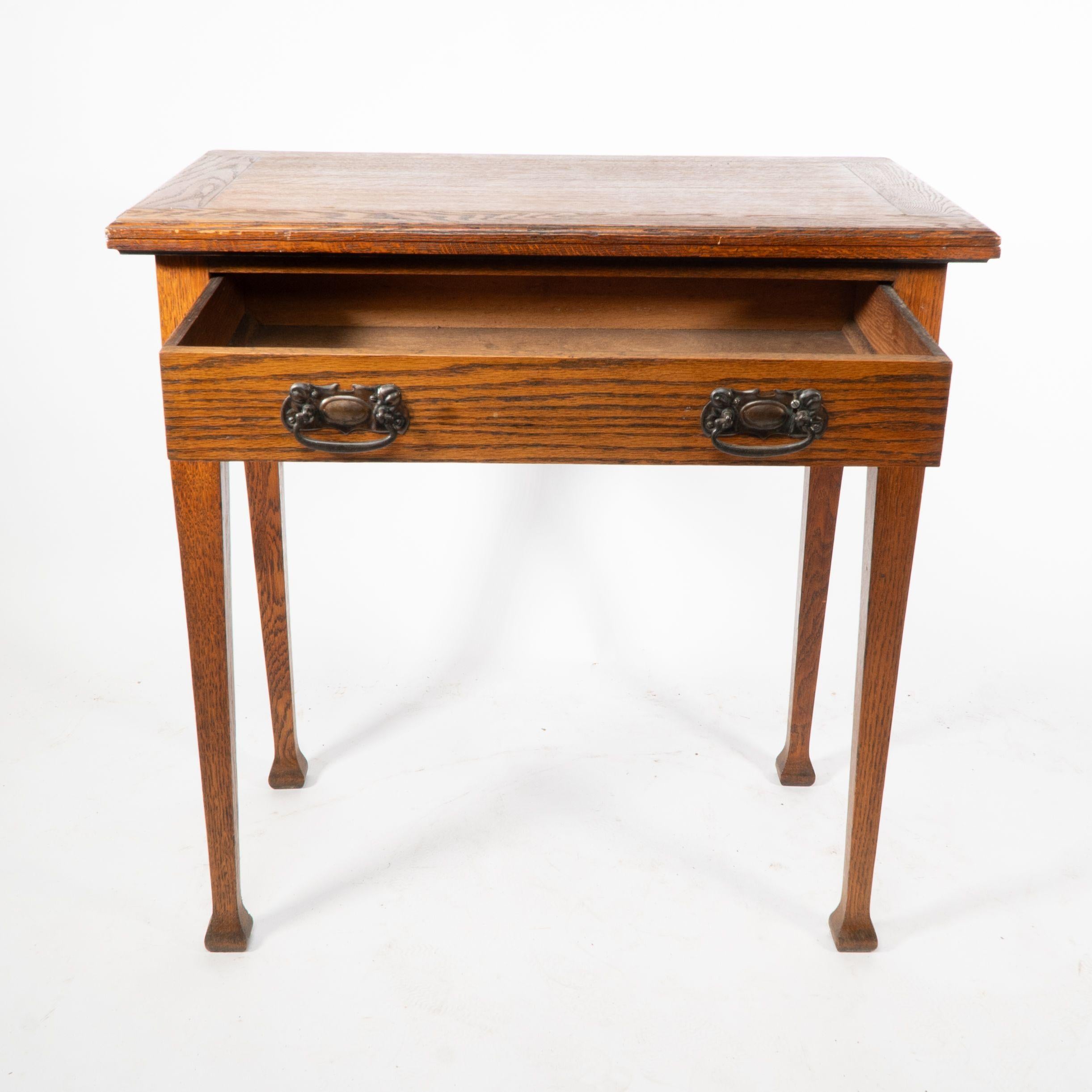 A good quality Arts and Crafts single drawer card/games table with stylised copper handles.