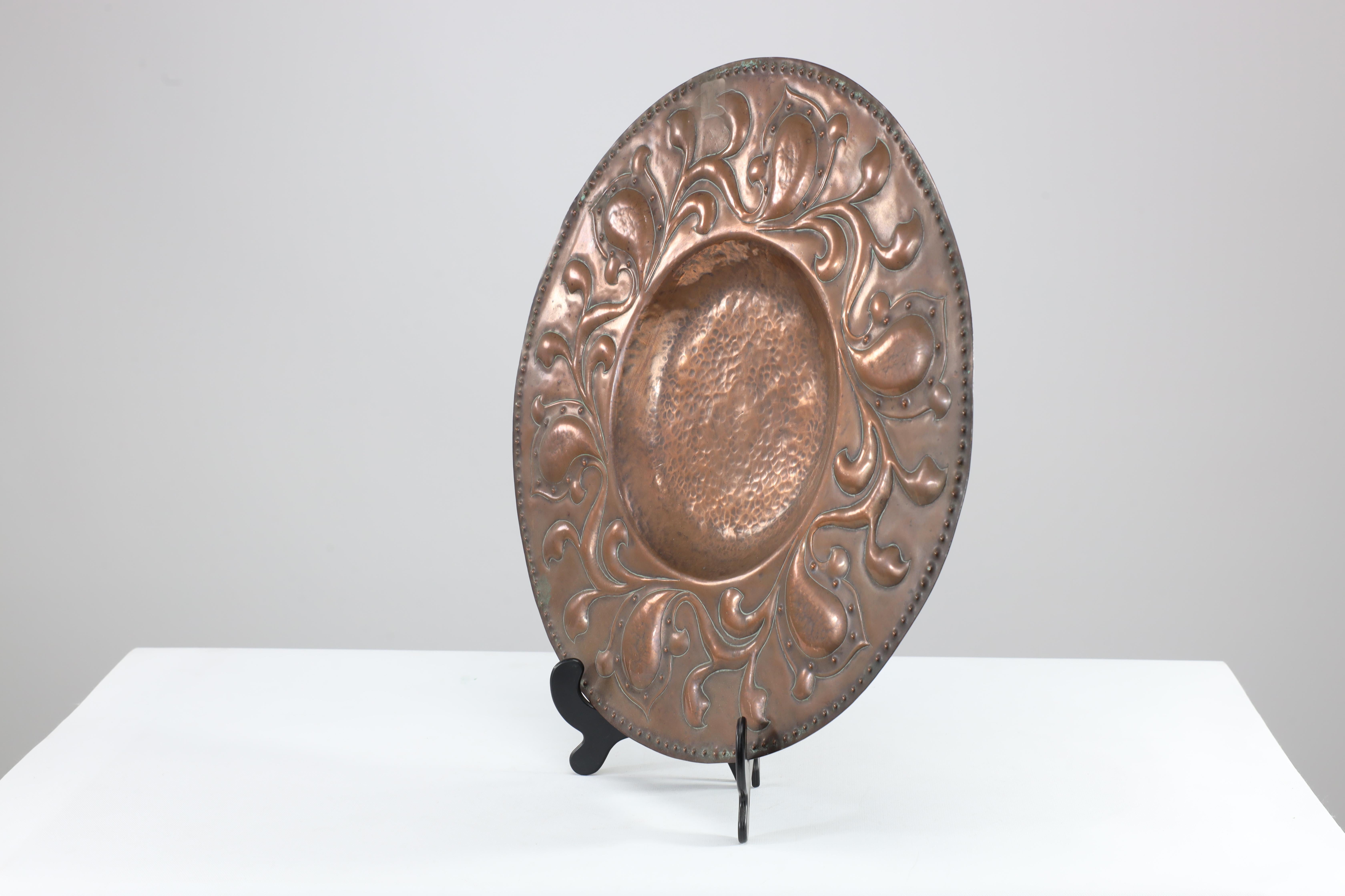 A good quality well executed Arts and Crafts copper wall plate with floral decoration and dot details emulating rivets around the centre.