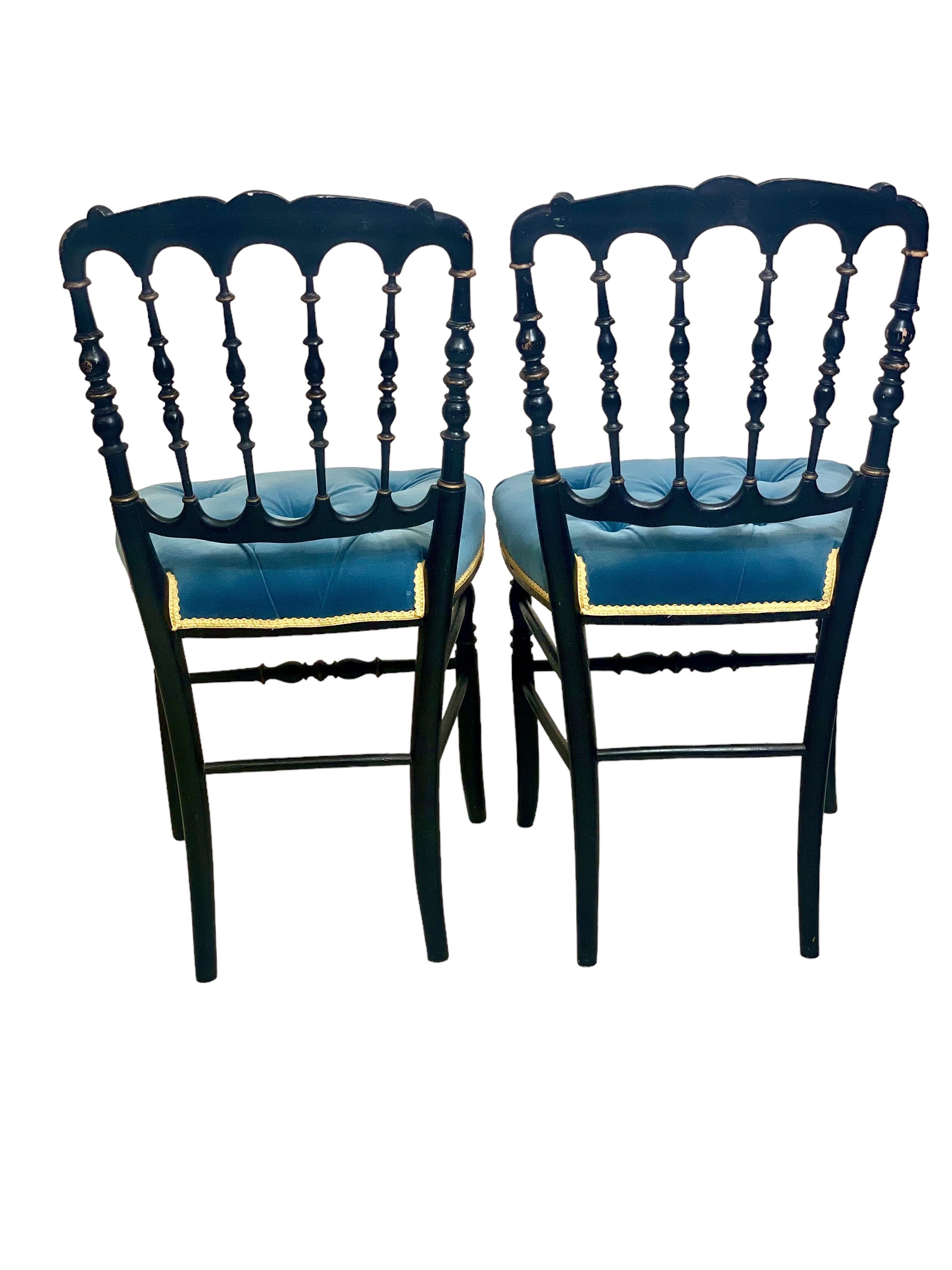 A gorgeous pair of 19th century Napoleon III opera chairs in ebonised wood, each with a wonderfully ornate spindle back and a gilded decoration of flowers and foliage on the top rail. A comfortable tufted seat in blue velvet is bound all round with