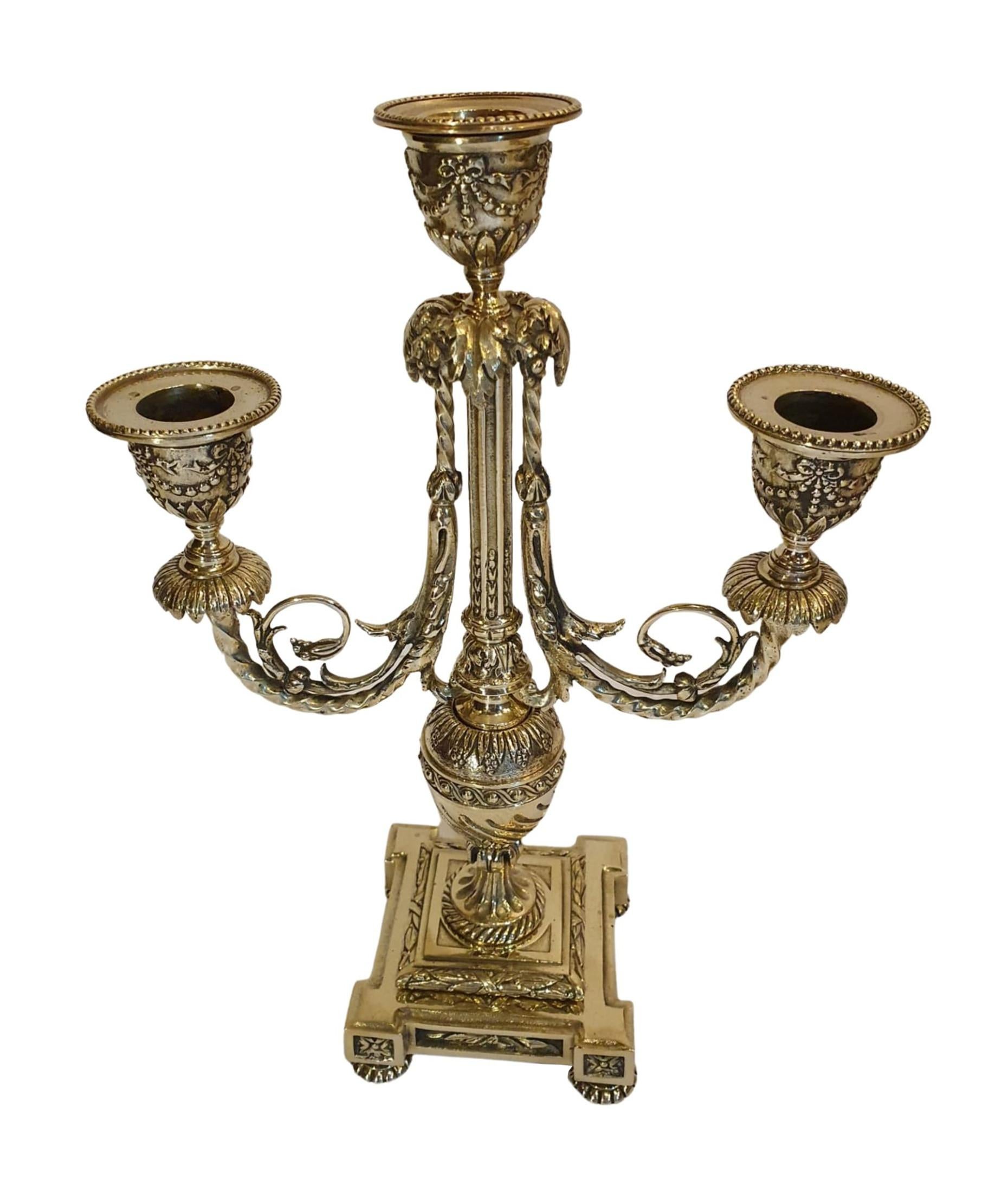 A gorgeous quality pair of 19th century polished brass three branch cande-labra, elaborately decorated with intricate ribbon, bow, scroll, guilloche and foliate motif detail throughout with fluted columnar and baluster stem sup-ported stepped plinth