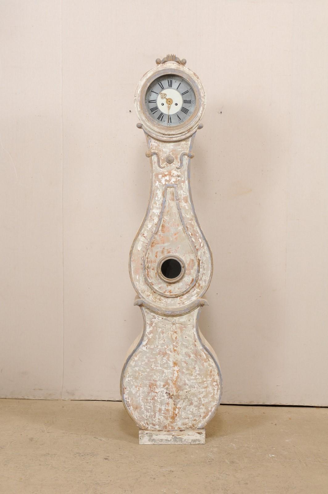 A 19th century Swedish Fryksdahl grandfather clock. This antique Fryksdahl clock from Sweden features a delicate crowned top, carved volute accents, which also adorn the neck area. The clock face has a particularly lovely (and original) face with