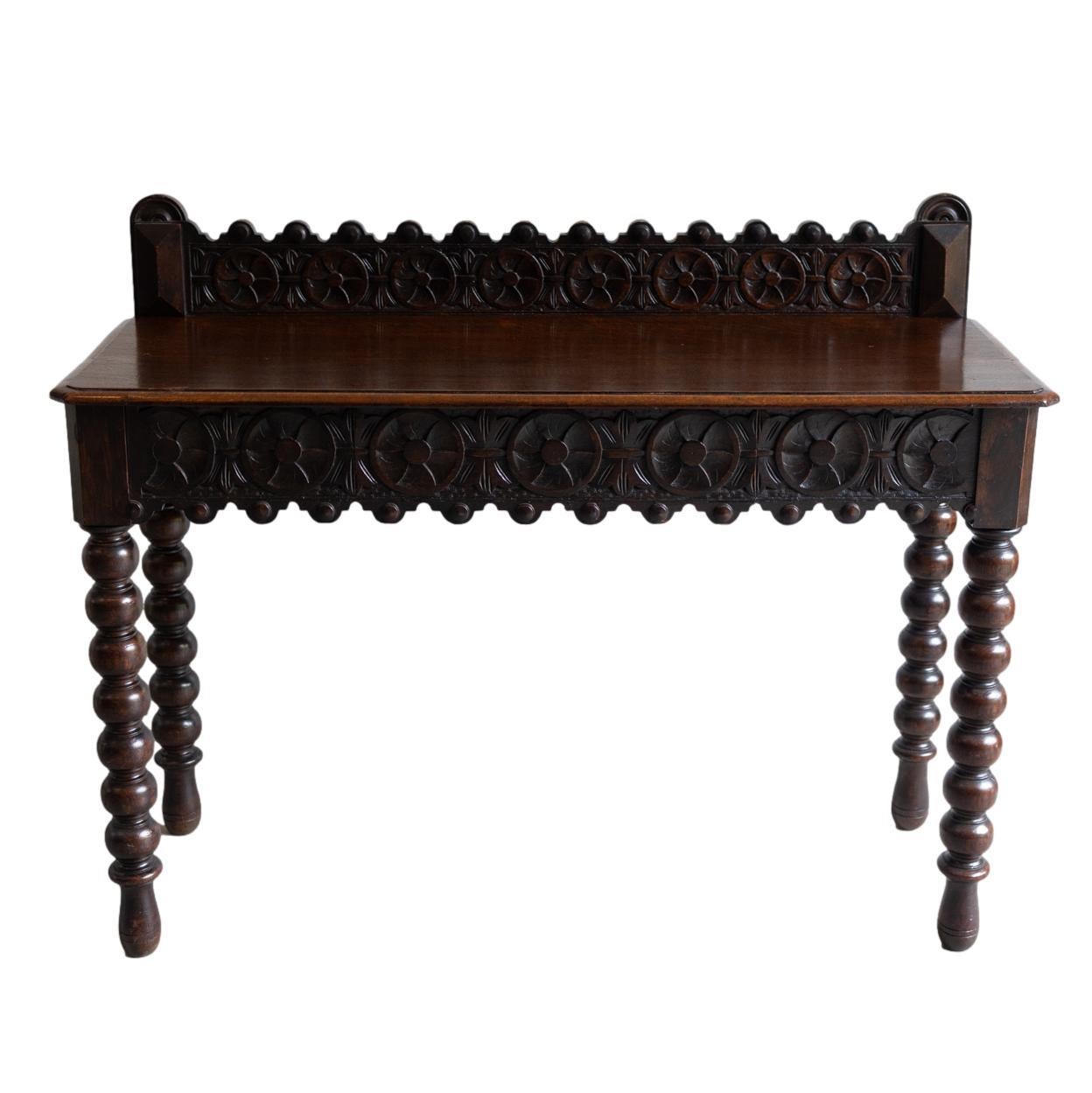 A Gothic Revival Hand-Carved Oak Console Table, elaborately carved with Gothic tracery, the top with canted corners, with a central hidden 16-inch frieze drawer, on bobbin-turned legs, English, ca. 1870.  