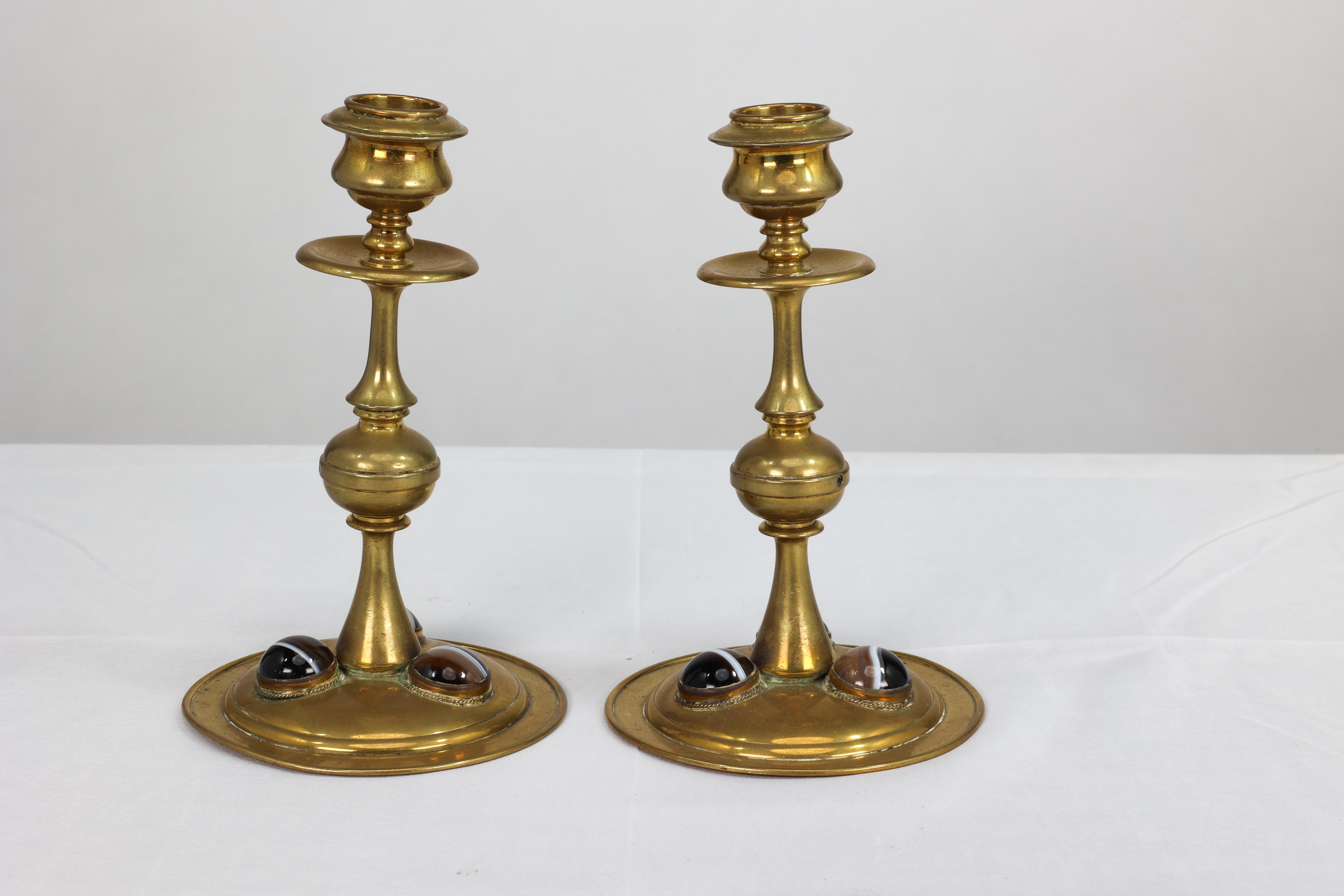 A Gothic Revival brass desk set with a pair of brass candlesticks and a matching pen tray all inset with multi-coloured semi-precious glass bulls eyes. Tray H 2.5 cm x W 22 cm x D 7.5 cm.