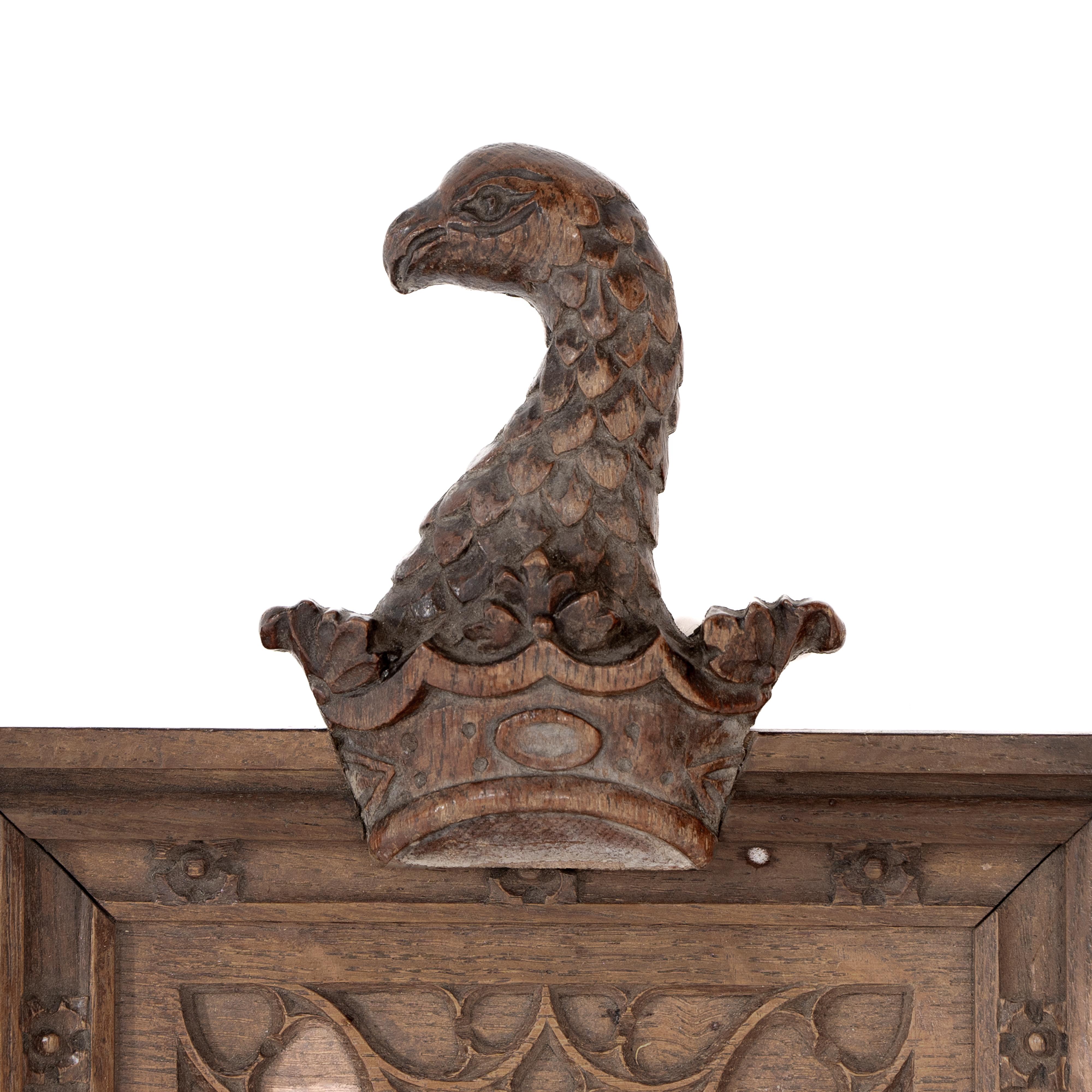 Ein neugotischer Eichenspiegel mit einem geschnitzten Adler auf der Oberseite und einem blinden gotischen Maßwerk darunter, das einen oberen Bogen bildet, die Seiten sind mit kleinen geschnitzten Röschen verziert. Der ursprüngliche Spiegel bleibt