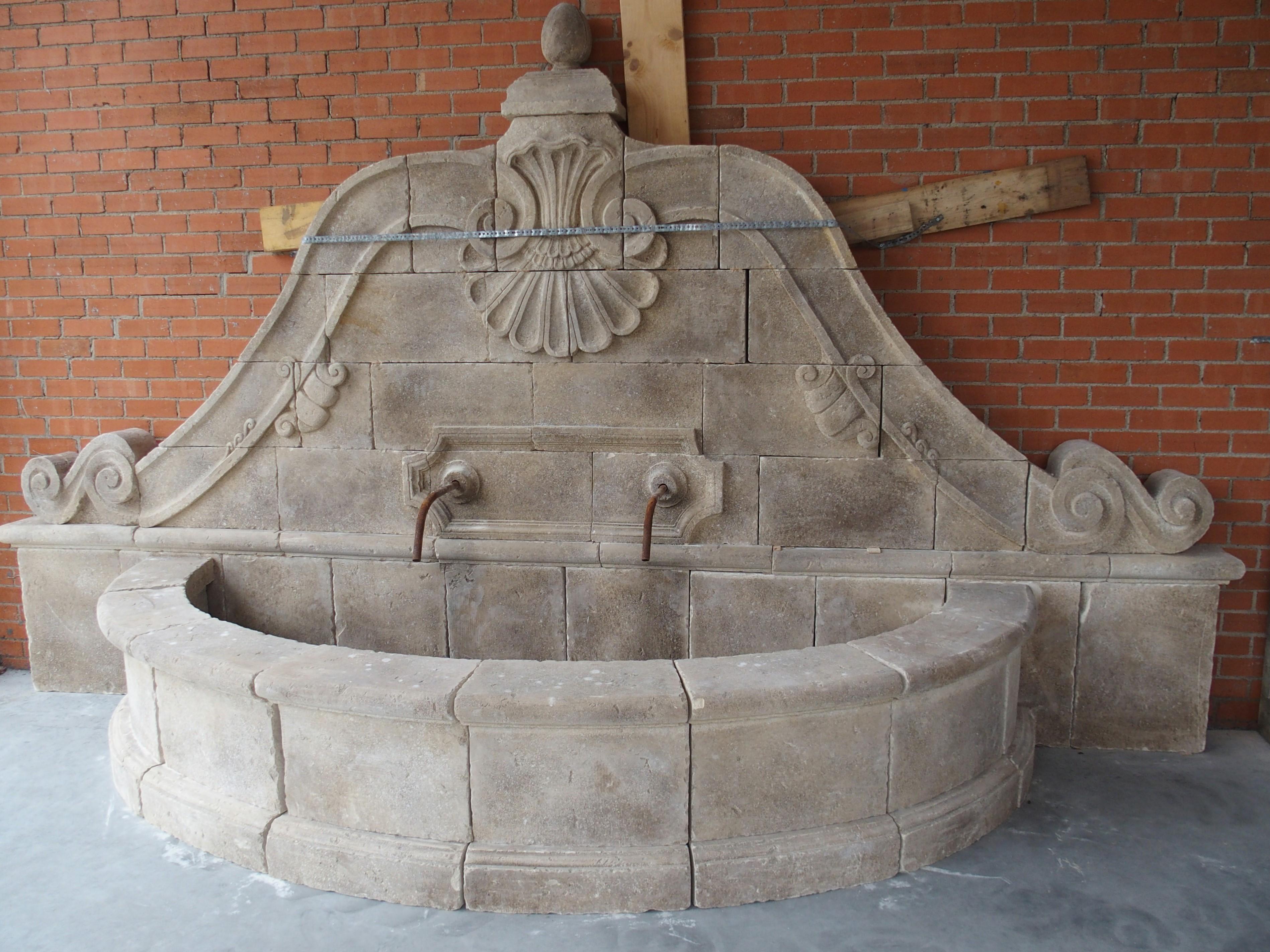 Dieser schöne Wandbrunnen mit zwei Ausläufern wurde in Italien aus 68 Kalksteinstücken handgeschnitzt. Der große Springbrunnen zeichnet sich durch sorgfältige Details aus, wobei die große, segmentierte Muschel, aus der sechs Steine der Rückwand
