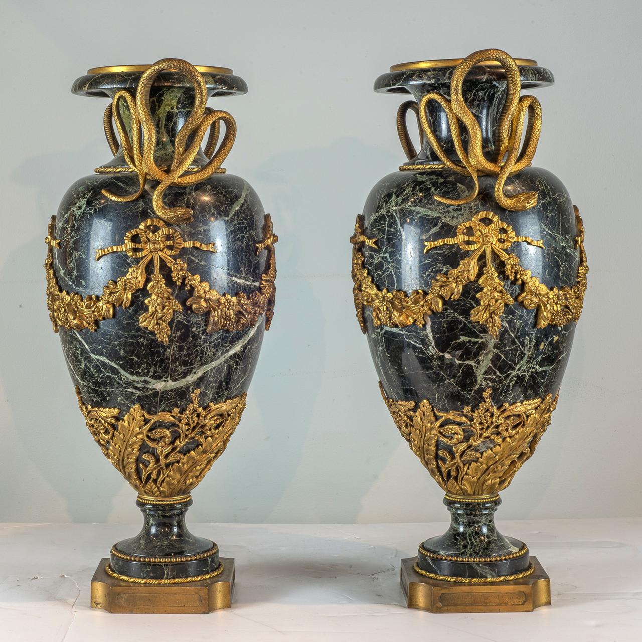 The grand and superb Ormolu-Mounted Verde Antico Marble Urns modeled with entwined serpent handles. The body applied with flowers swags jointed by a bow and the fluted foot is covered by an elaborate decoration.

Origin: French
Date: 19th