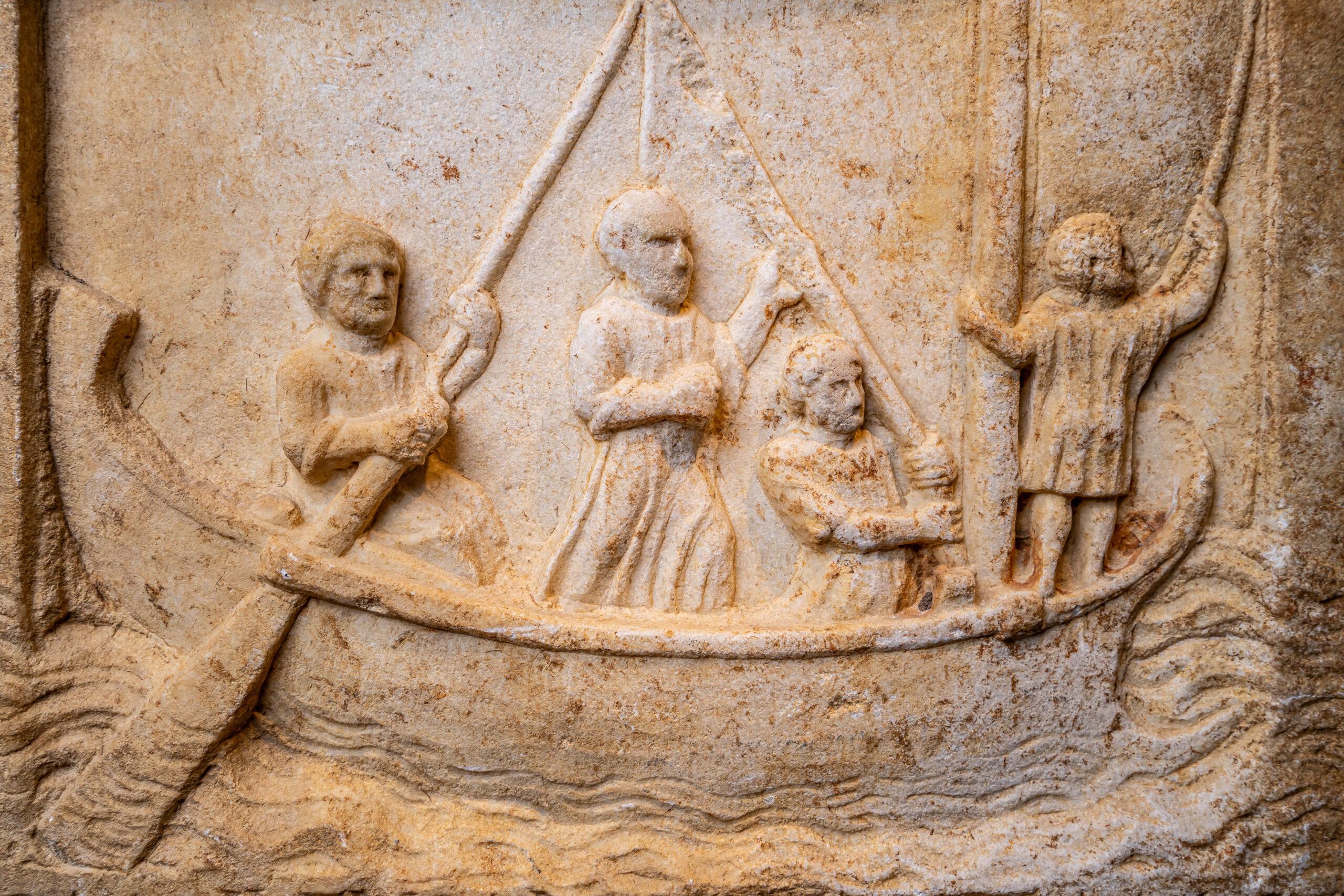 Stèle funéraire en marbre grec, en forme de naiskos, le fronton avec un rondeau central et des acrotères aux angles, avec une scène sculptée en haut relief dans une niche rectangulaire, flanquée de colonnes, représentant un bateau sur une mer