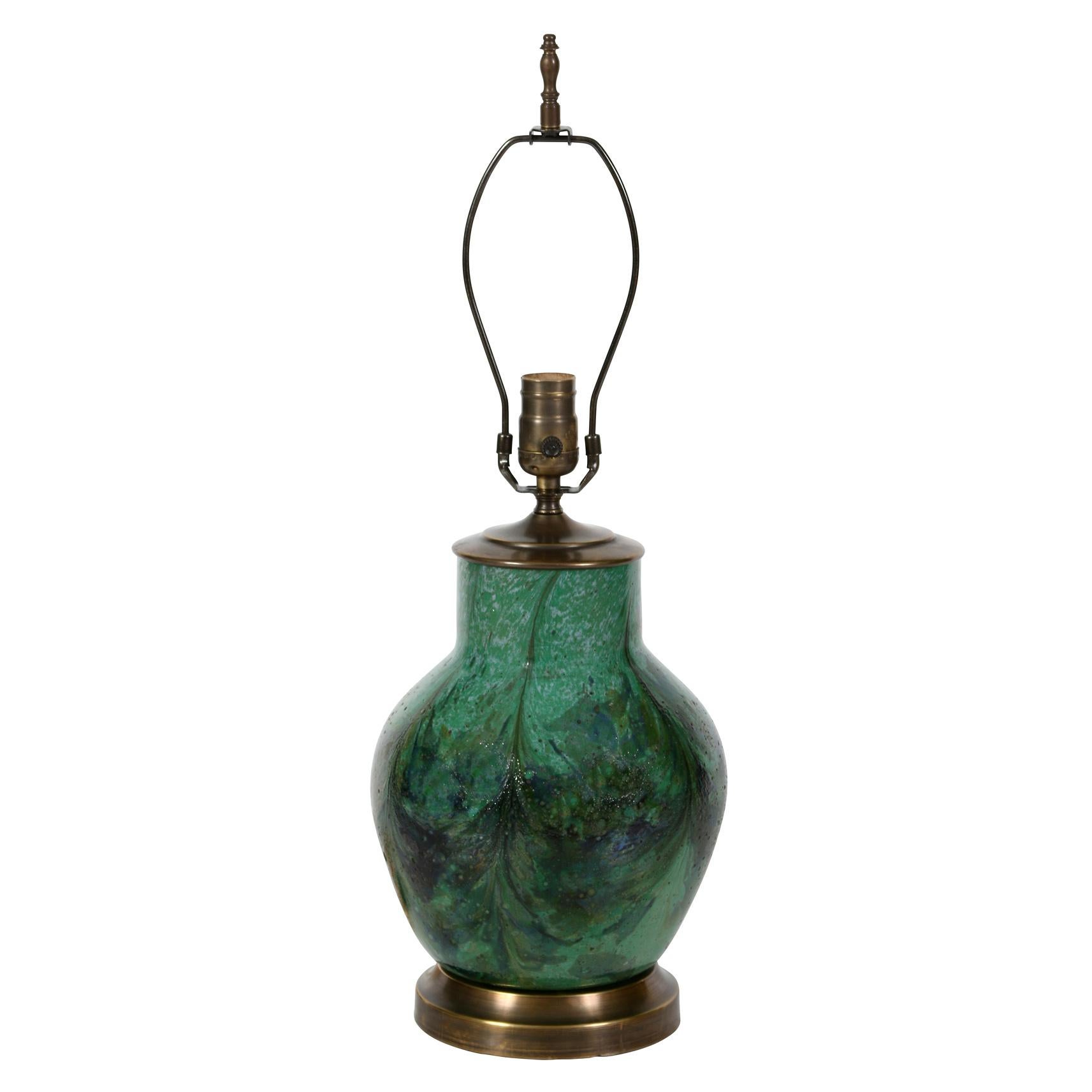 Cette lampe en céramique verte de style asiatique se distingue par sa belle glaçure.  Dans différentes teintes de verts et de bleus, la glaçure a presque un effet marbré.  Montée sur une base en laiton, la lampe est dotée d'un abat-jour plissé en