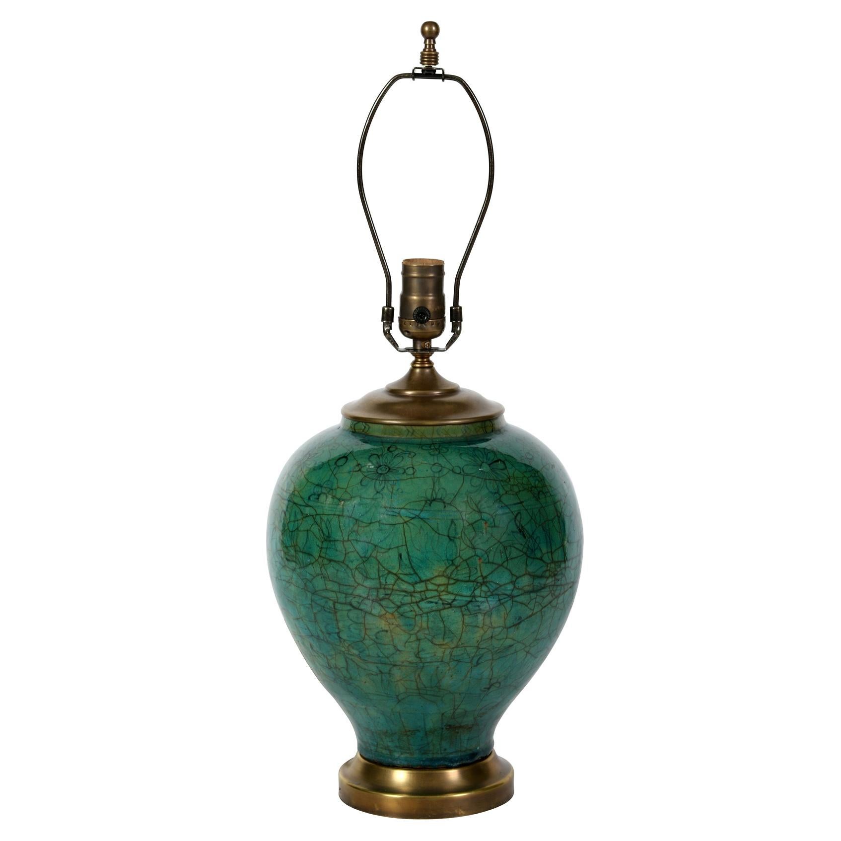 A green ceramic lamp in the Asian style, with a crackled glaze in a deep jade green.  Mounted on a brass base, the lamp has a pleated linen shade.
