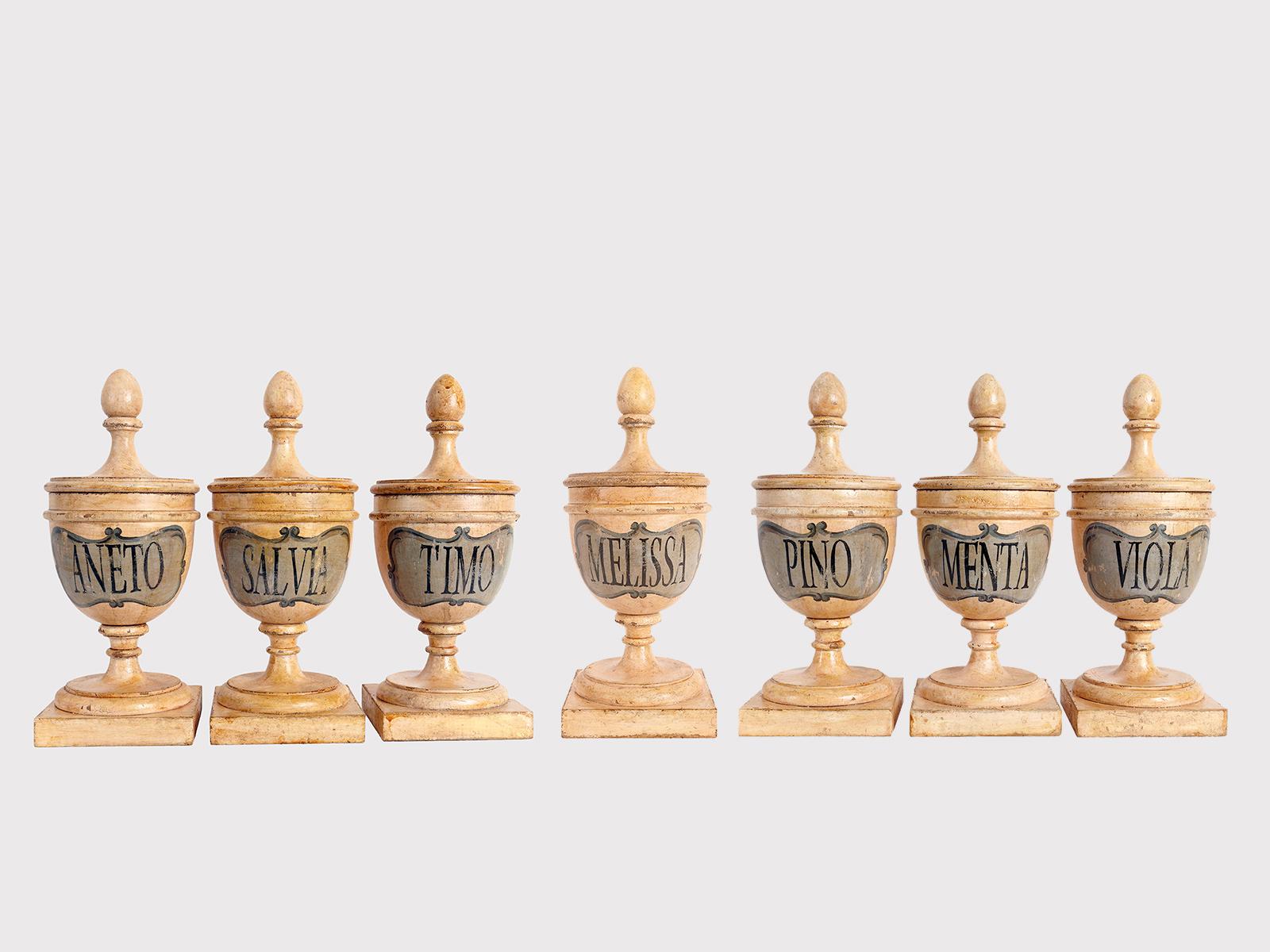 Set of seven medium-sized fruitwooden pharmacy-herbal jars (Pine, Mint, Viola, Melissa, Dill, Sage, Thyme) in the purest neoclassical style. The surface is finished with a white pad with a blue scroll decoration, the names of the herbs in black.