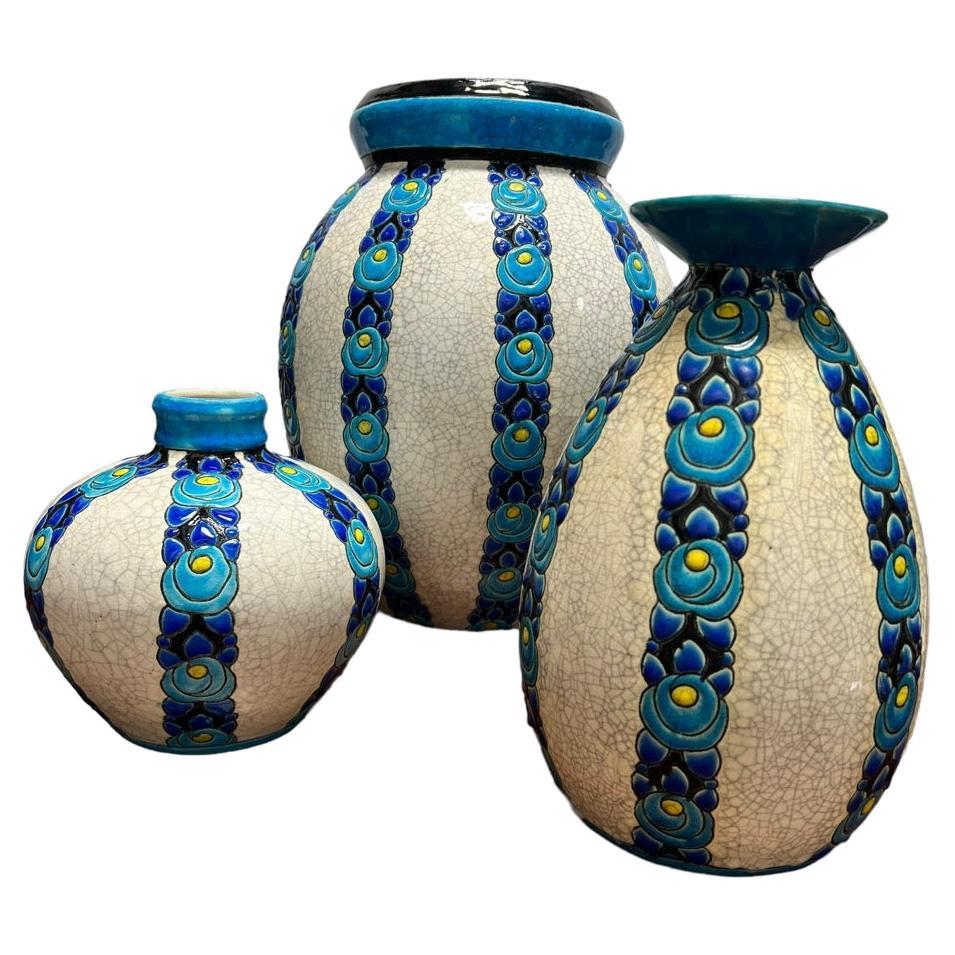Voici un trio captivant de vases à fleurs bleus des années 1920, animés par le génie artistique de Charles Catteau (1880-1966) dans une exquise faïence émaillée. Chacun de ces vases exceptionnels porte un numéro unique et arbore fièrement la marque