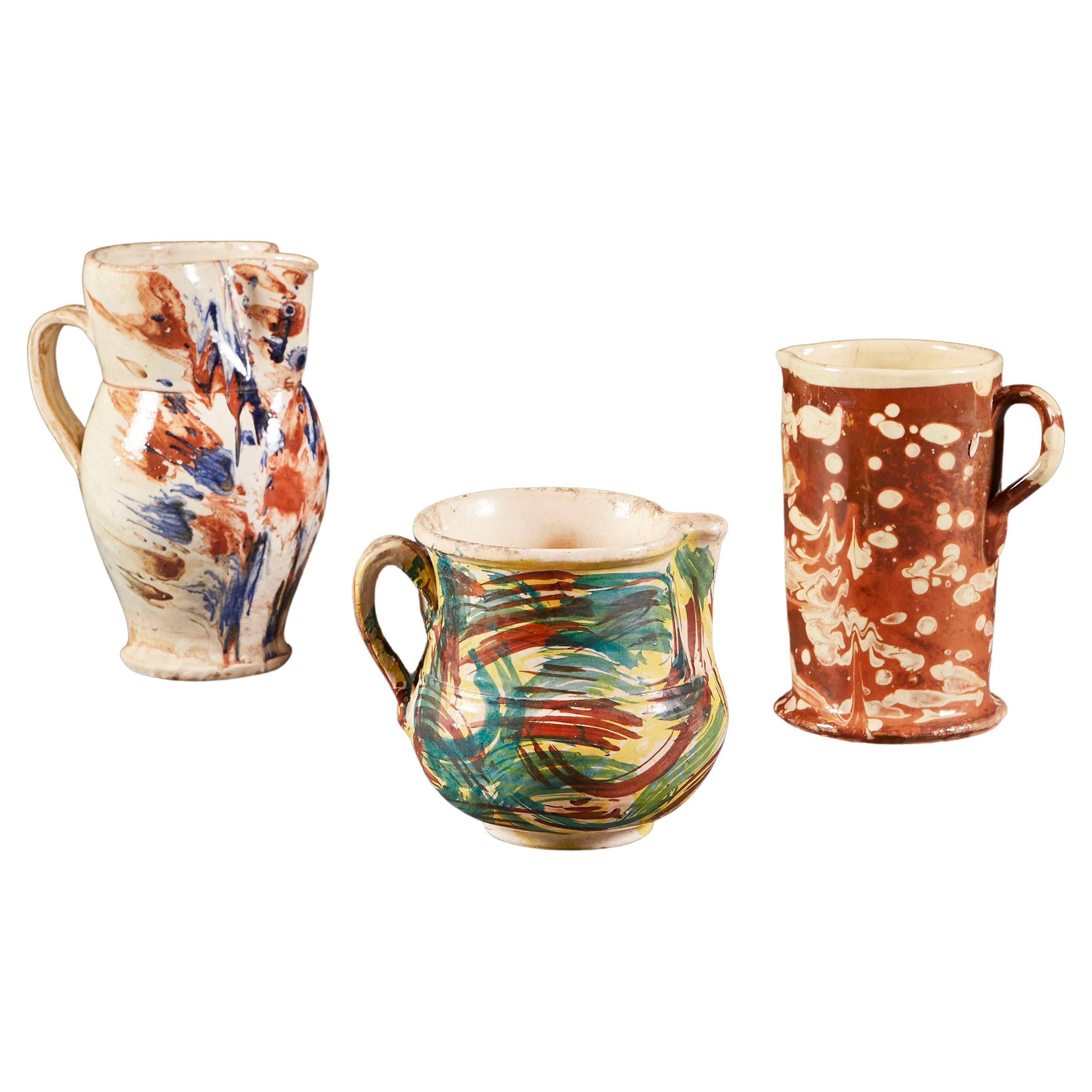 A group of three mid nineteenth century Italian jugs. One with sienna and cream marbleised glaze, two with polychrome, abstract designs hand painted with loose, expressive brushstrokes prior to glazing.

  
 