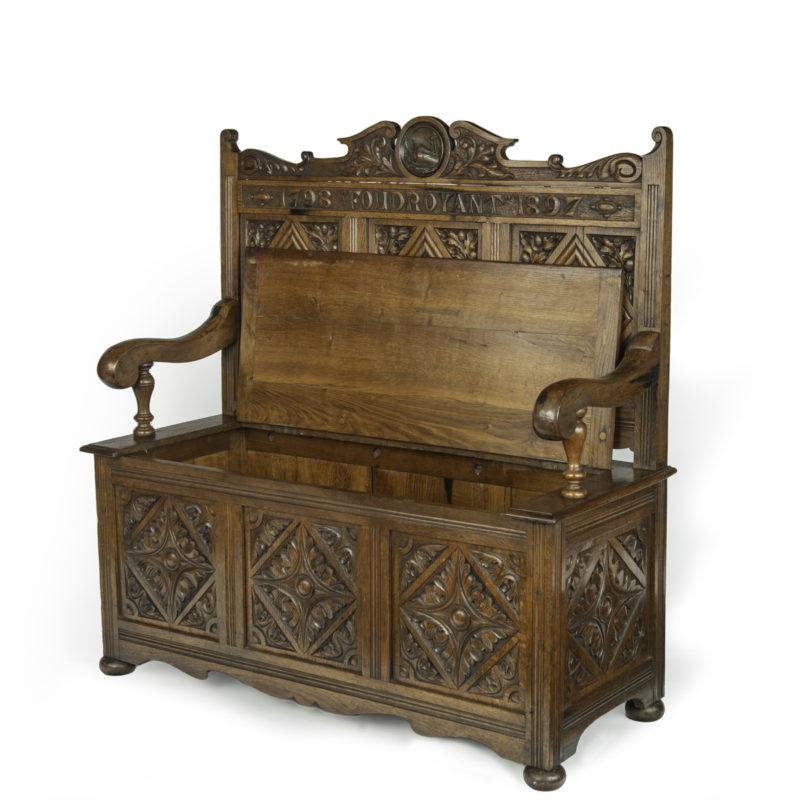 A hall bench made from the timbers of H.M.S. Foudroyant, 1897 This ornate oak hall bench is by Goodall, Lamb and Heighway.  It is of rectangular form with a solid back surmounted by a broken pediment enclosing a copper roundel showing Foudroyant