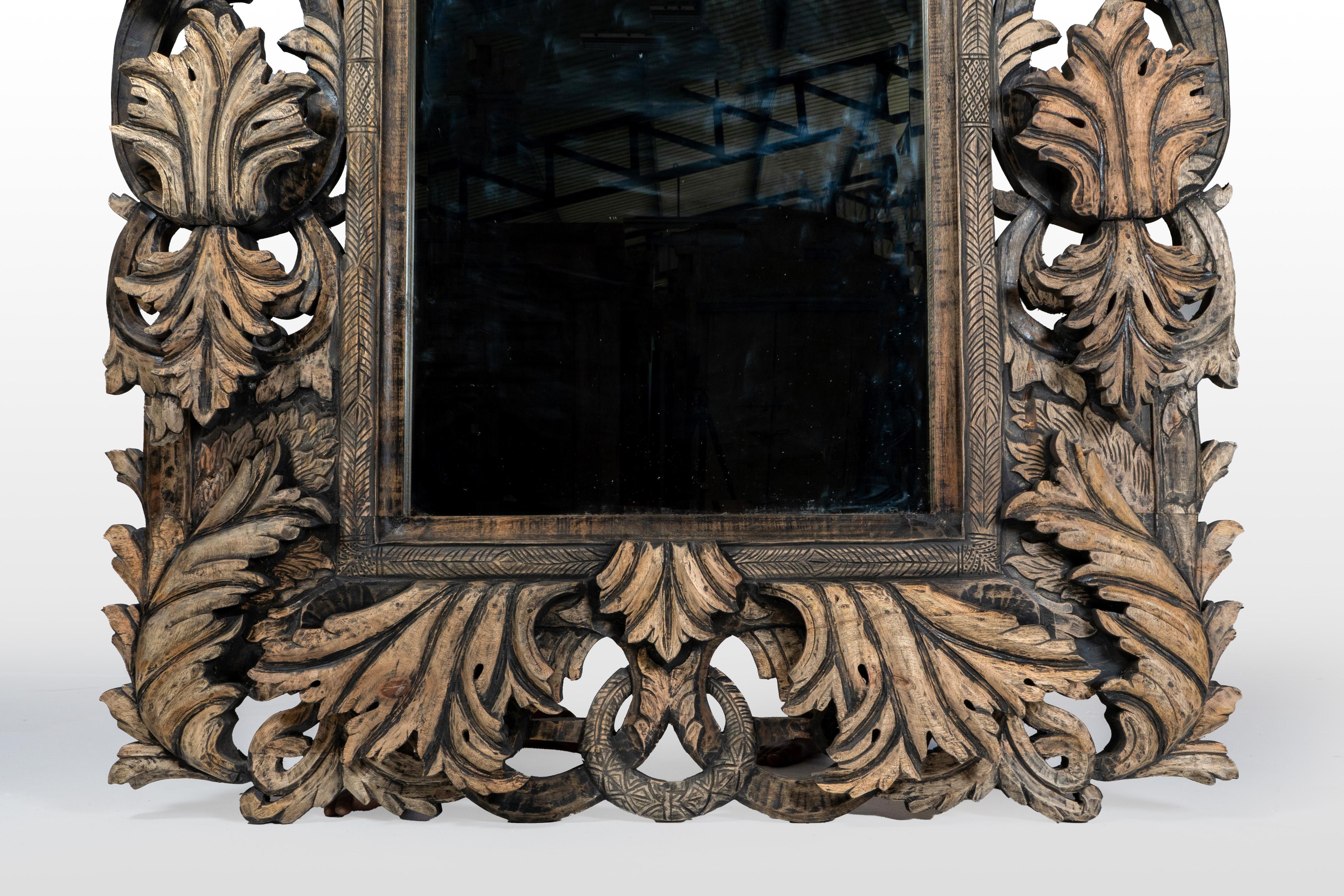 This impressive contemporary Indian wood mirror frame beautifully blends Indo-European stylistic elements, showcasing intricate craftsmanship and exquisite detailing. The frame seamlessly merges traditional Indian motifs of elaborate mango leaves