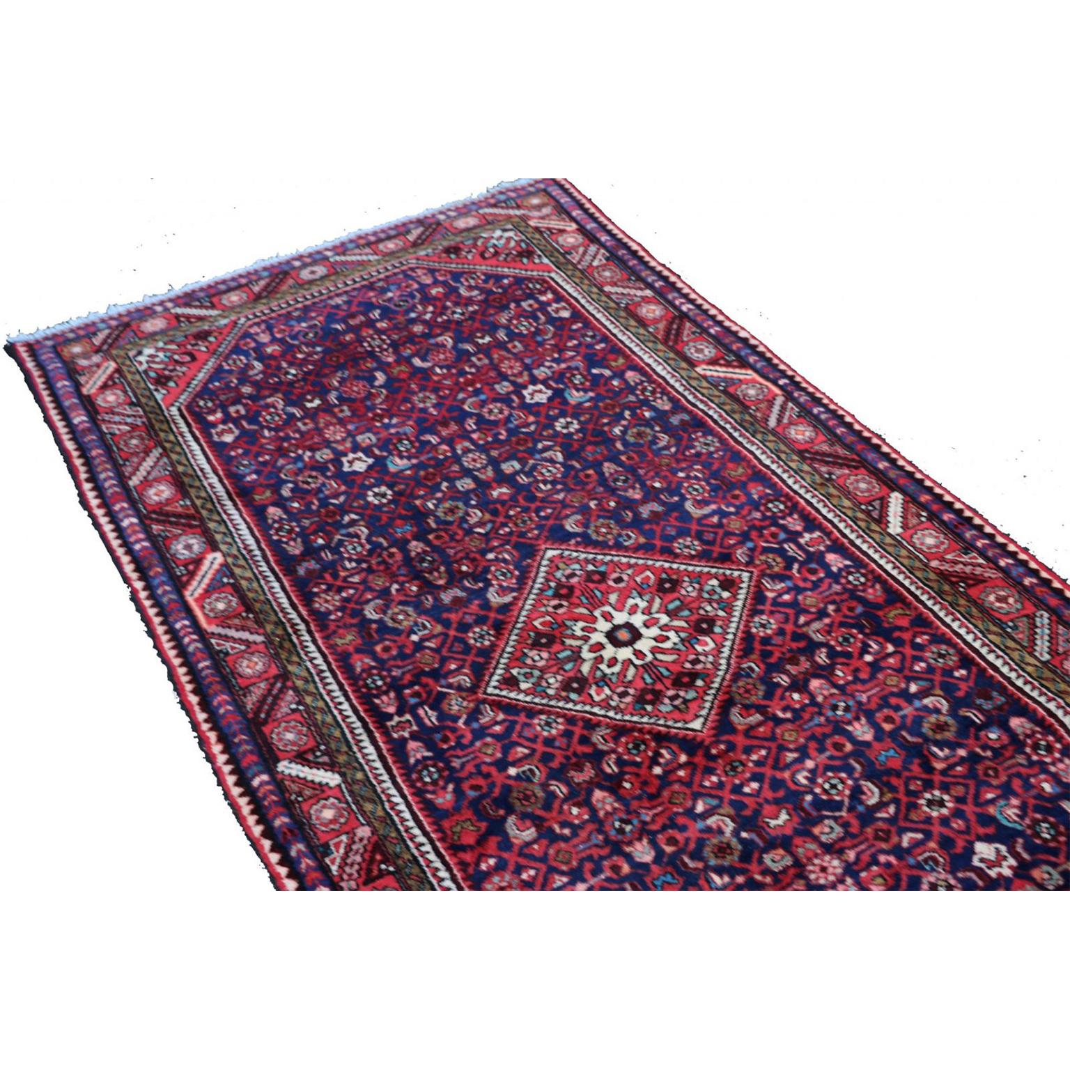 A hand knotted wool Hamadan rug, North West Persia, wool on cotton foundation. The blue field with a central diamond lozenge floral medallion supported by all-over “Herati”, within a red paneled flower head and alternating stepped leaf