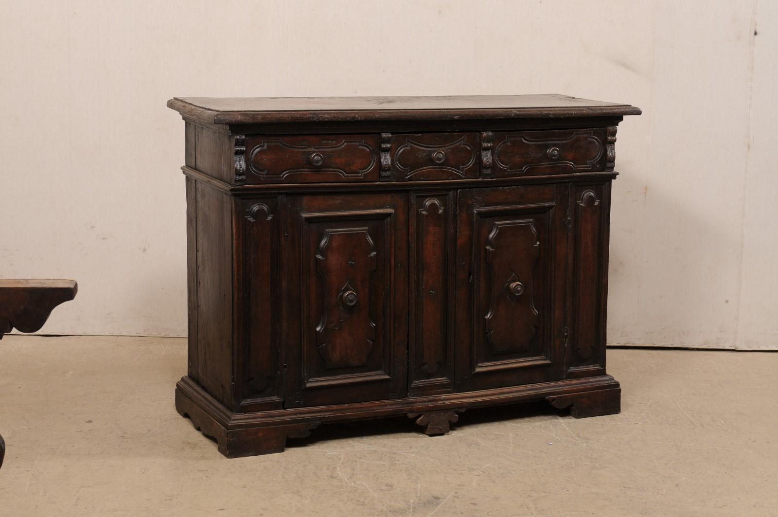 An Italian carved walnut wood buffet credenza from the 18th century. This antique sideboard from Italy features rich walnut wood which has been carved with raised decorative cartouche plaques, in varying designs, about the front face. This piece has