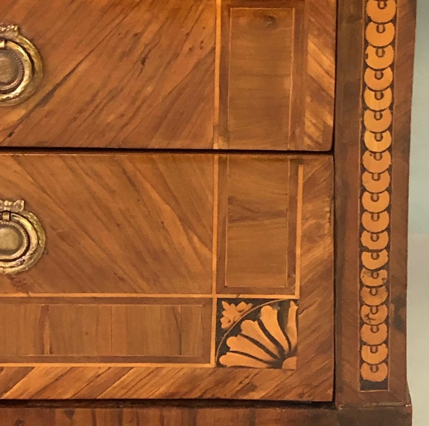 Of mixed woods with marquetry and parquetry inlay; the rectangular top with large central reserve within a cross-banded border; the body fitted with 3 long drawers with herring-bone veneer adorned with spandrels and imbricated decoration with