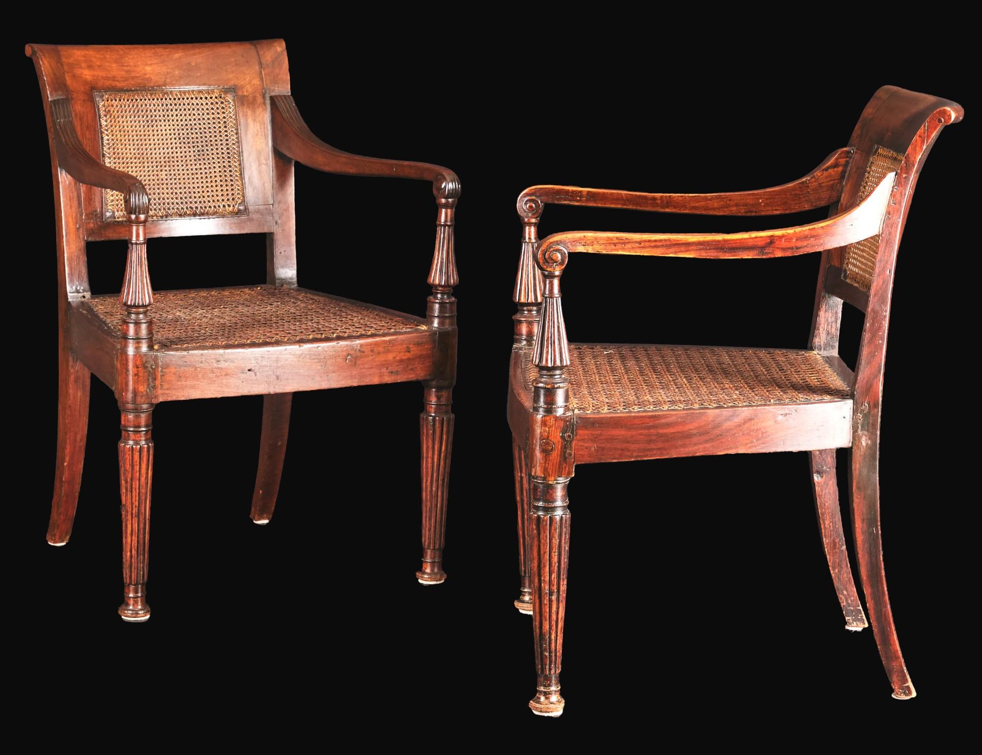 A very handsome pair of 19th century Anglo-Indian armchairs, showing richly figured padouk wood frames of pegged construction, with caned backs & seats sided by swept armrest atop flaring & reeded supports, raised overall on reeded front supports