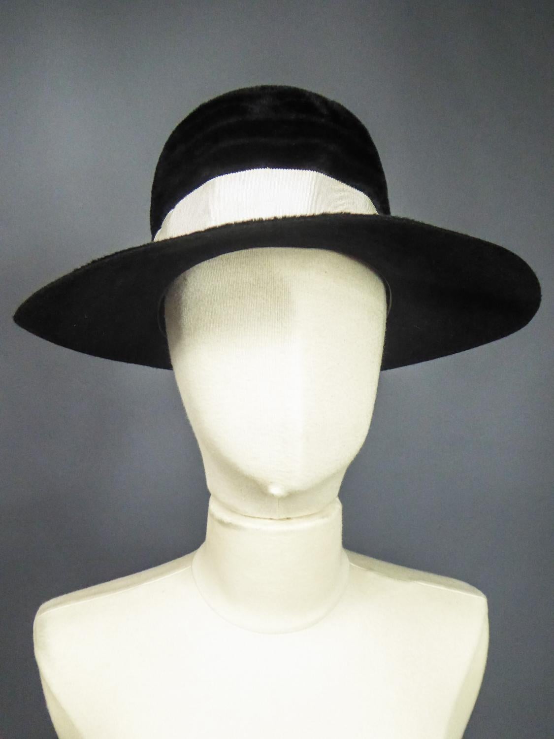 Circa 1970
Inghilterra
Cappello da collezione in feltro a coste con bande concentriche in peluche dell'Atelier Lucas per Harrods, un famoso negozio di lusso londinese degli anni '70. Cappello con calotta alta e rotonda, ampi bordi modellabili e