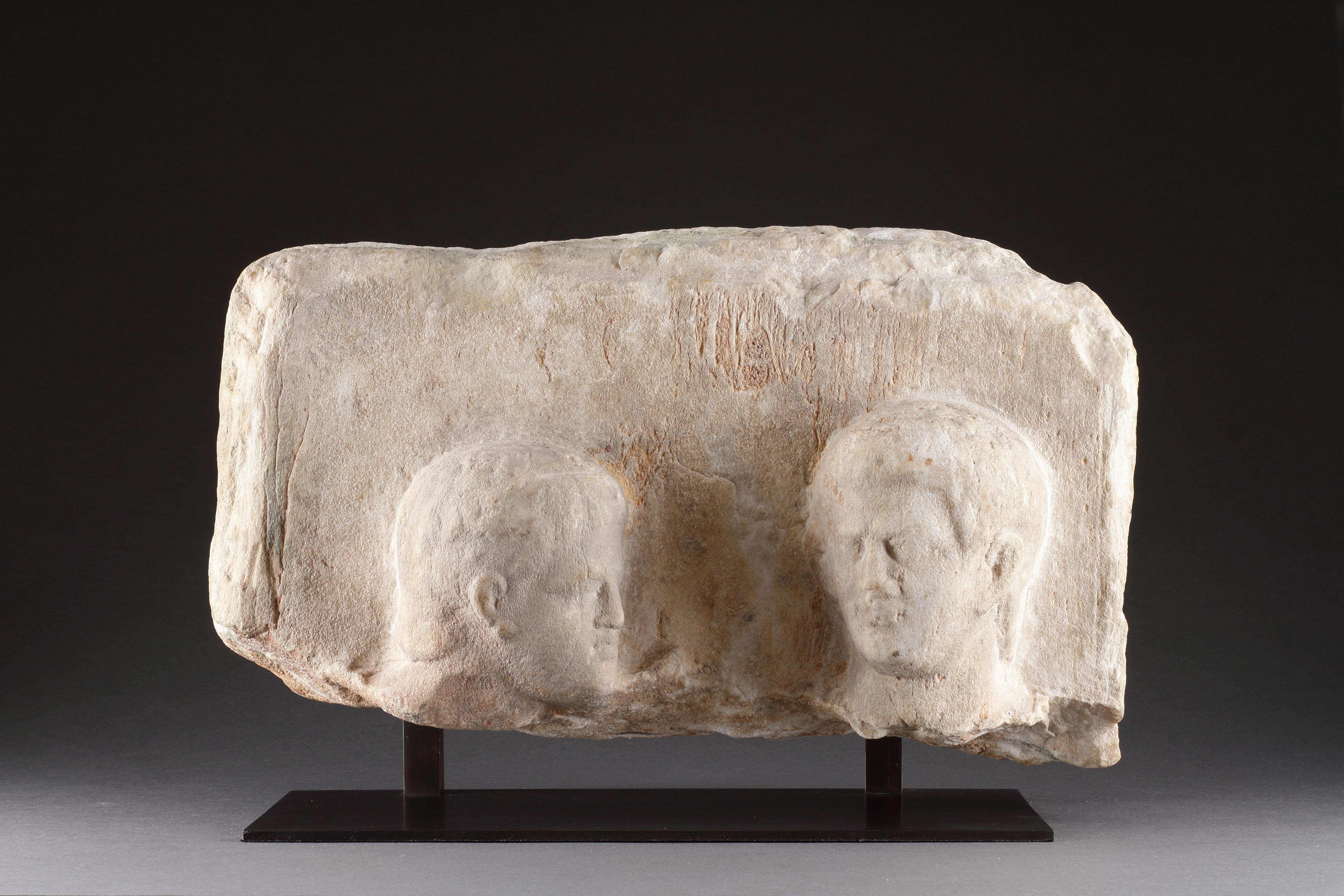 A Hellenistic Funerary Stele in High Relief with Two Male Heads 
Marble 
Greek Hellenistic 
Circa 2nd Century BC

Size: 20.5cm high, 38cm wide, 11cm deep - 8 ins high, 15 ins wide, 4¼ ins deep / 25.5cm high - 10 ins high (with base)

Provenance: 
Ex
