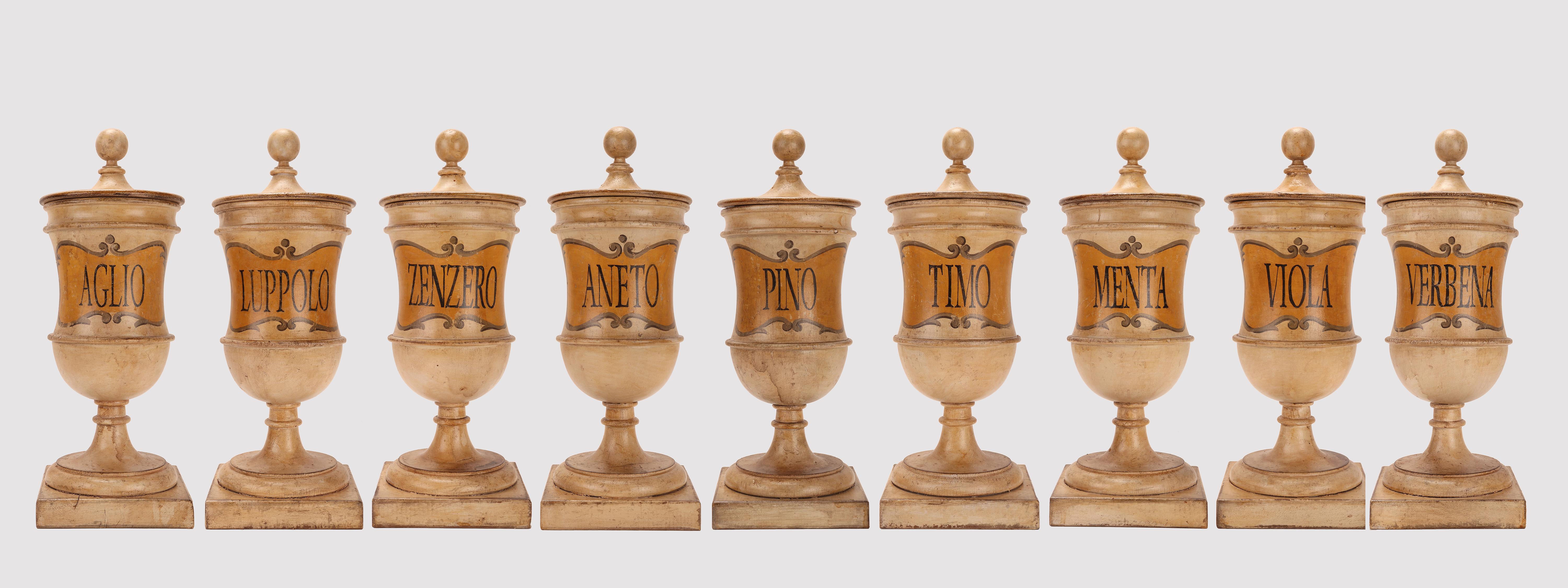 Set of 3 (of nine) big herbalist apothecary wooden jars (mint leaves, verbena flowers, viola flowers), in the purest Neoclassical style. The surface is finished with pastiglia white-cream with saffron color cartouche and gold decoration finishing