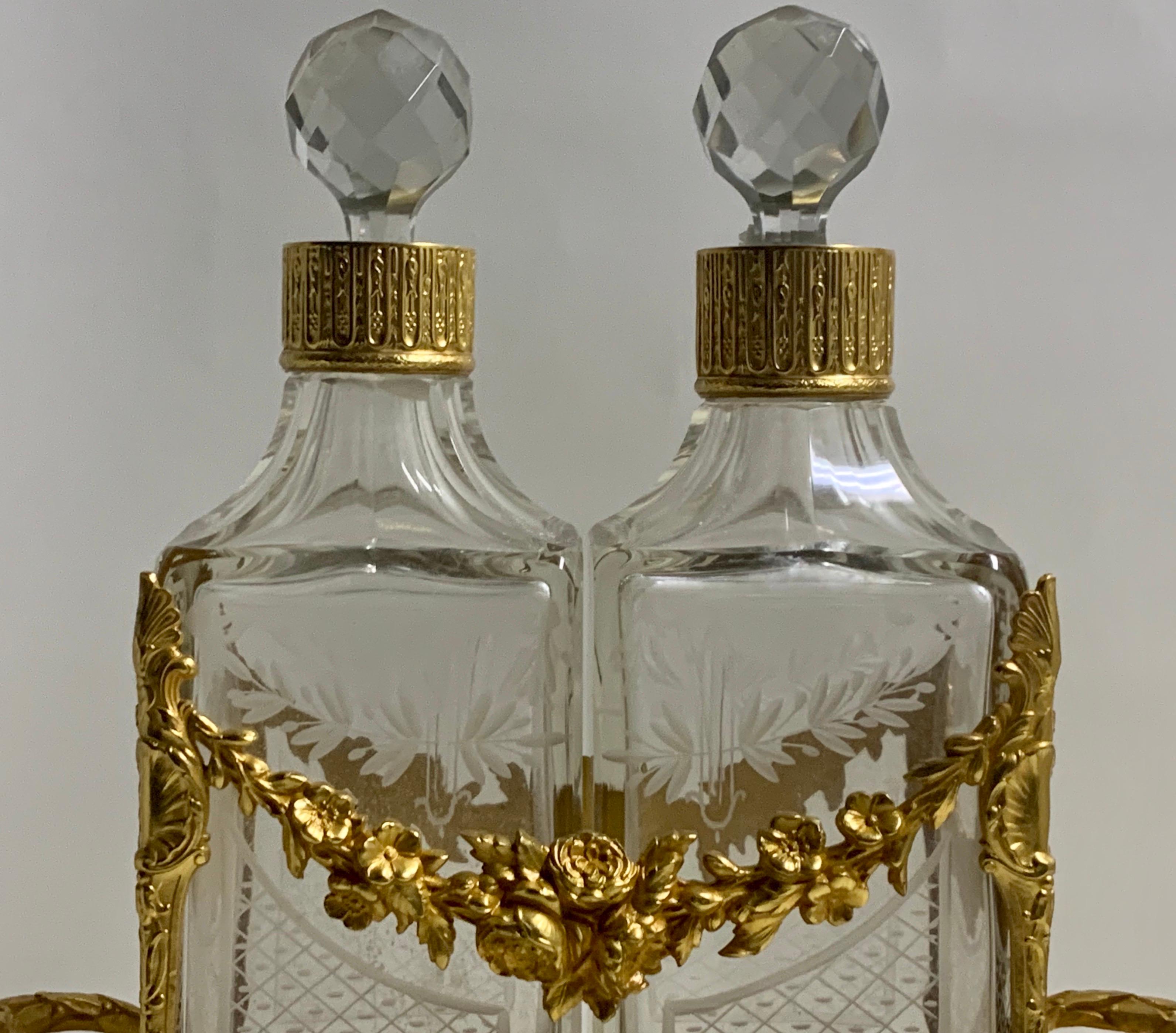A late 19th century French gilt bronze decanter caddy/stand. The stand marked France the pierced foliate-cast stand flanked by Fasces Handles, with two cut and etched crystal decanters with faceted stoppers overall 10 3/4'' x high x 8'' W x 3.1/4''