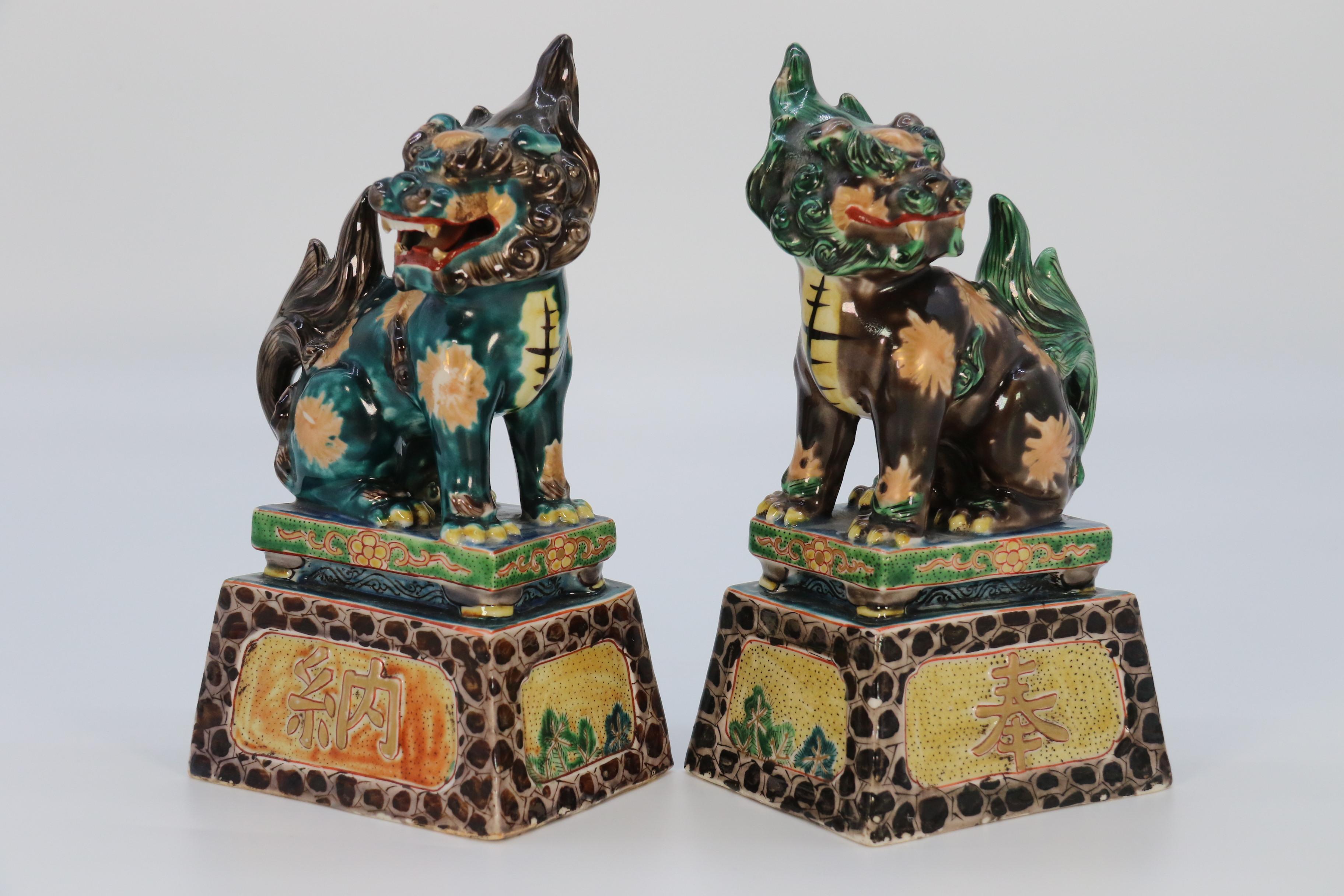 An unusual pair of 19th century Chinese hand painted and richly glazed pottery seated Buddhist lions. They are each raised onto a stepped plinth with gilt character marks on the front face with bamboo and foliage around the sides and back on pale