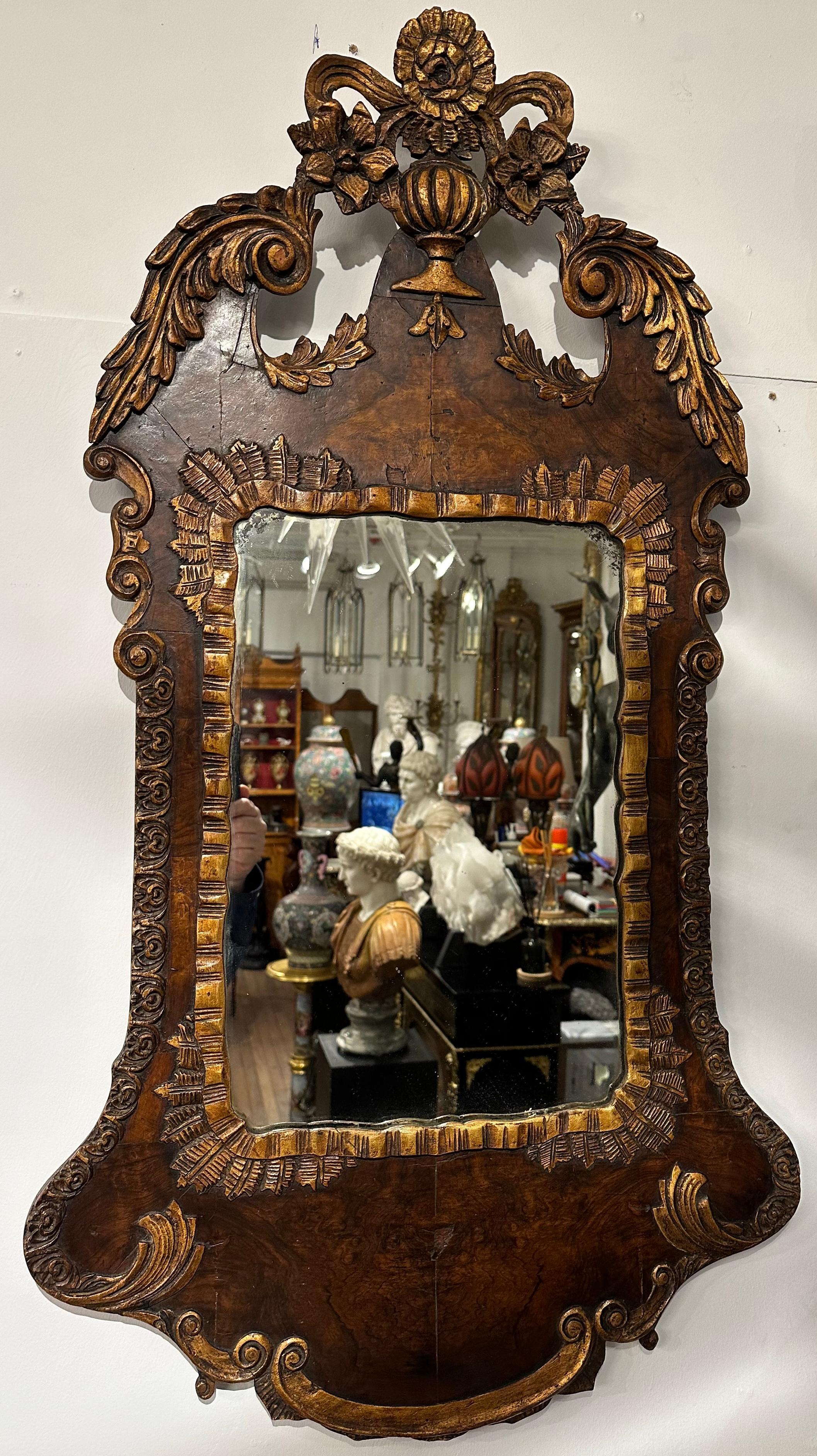 A pair of highly decorative hand carved and gilded walnut frame mirrors. Featuring a crest with floral gilded carving and elaborate ribbon gilding around the glass. These mirrors would look imposing in any setting. 