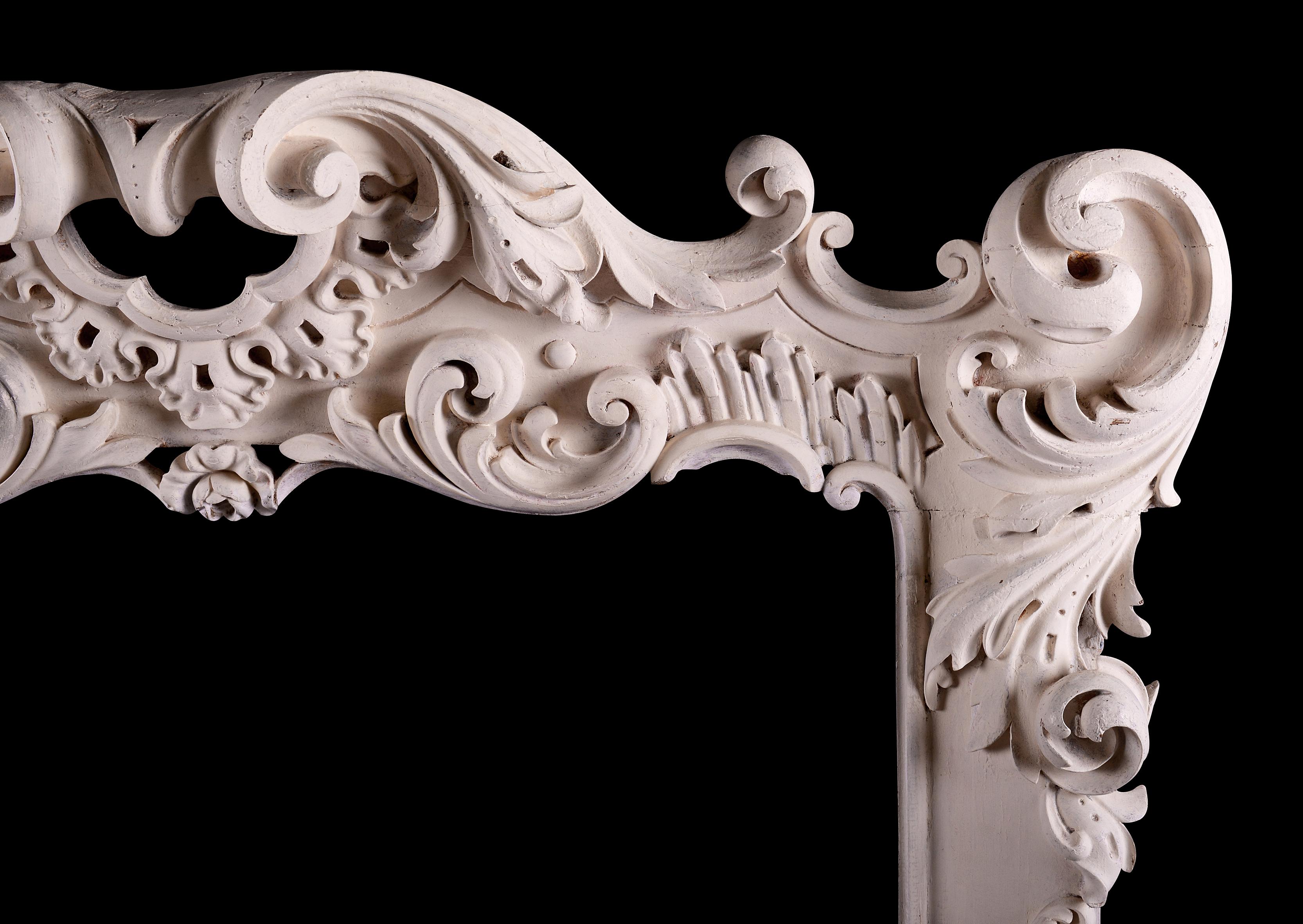 A highly decorative French Rococo wood fireplace. The jambs with scrollwork throughout surmounted by frieze with scrolls, floral embellishments and cartouche to centre. French. Currently painted in rustic style, but could be stripped if required for