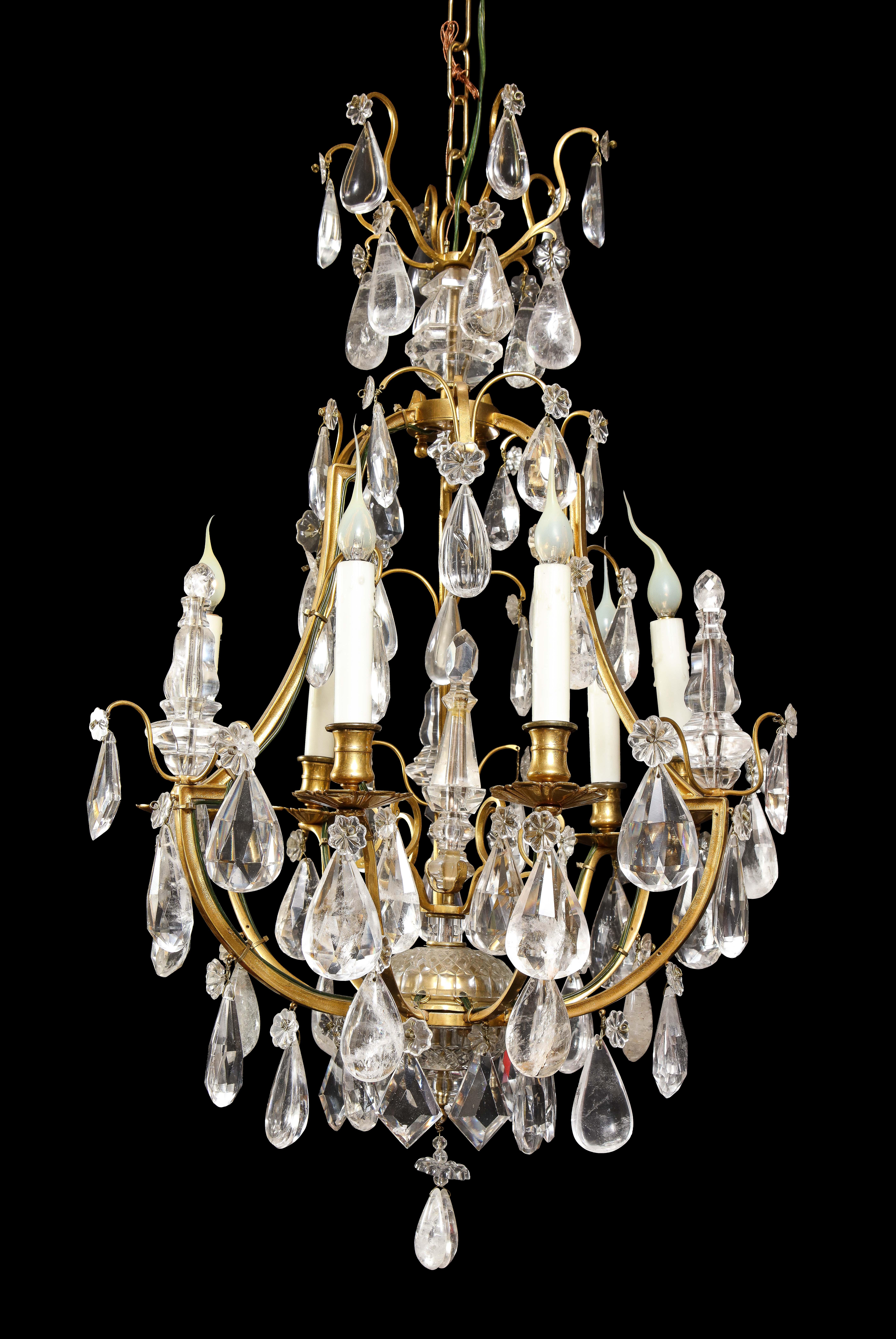 A Hollywood Regency style gilt bronze and cut rock crystal cage form multi light chandelier embellished with cut rock crystal obelisks and prisms.