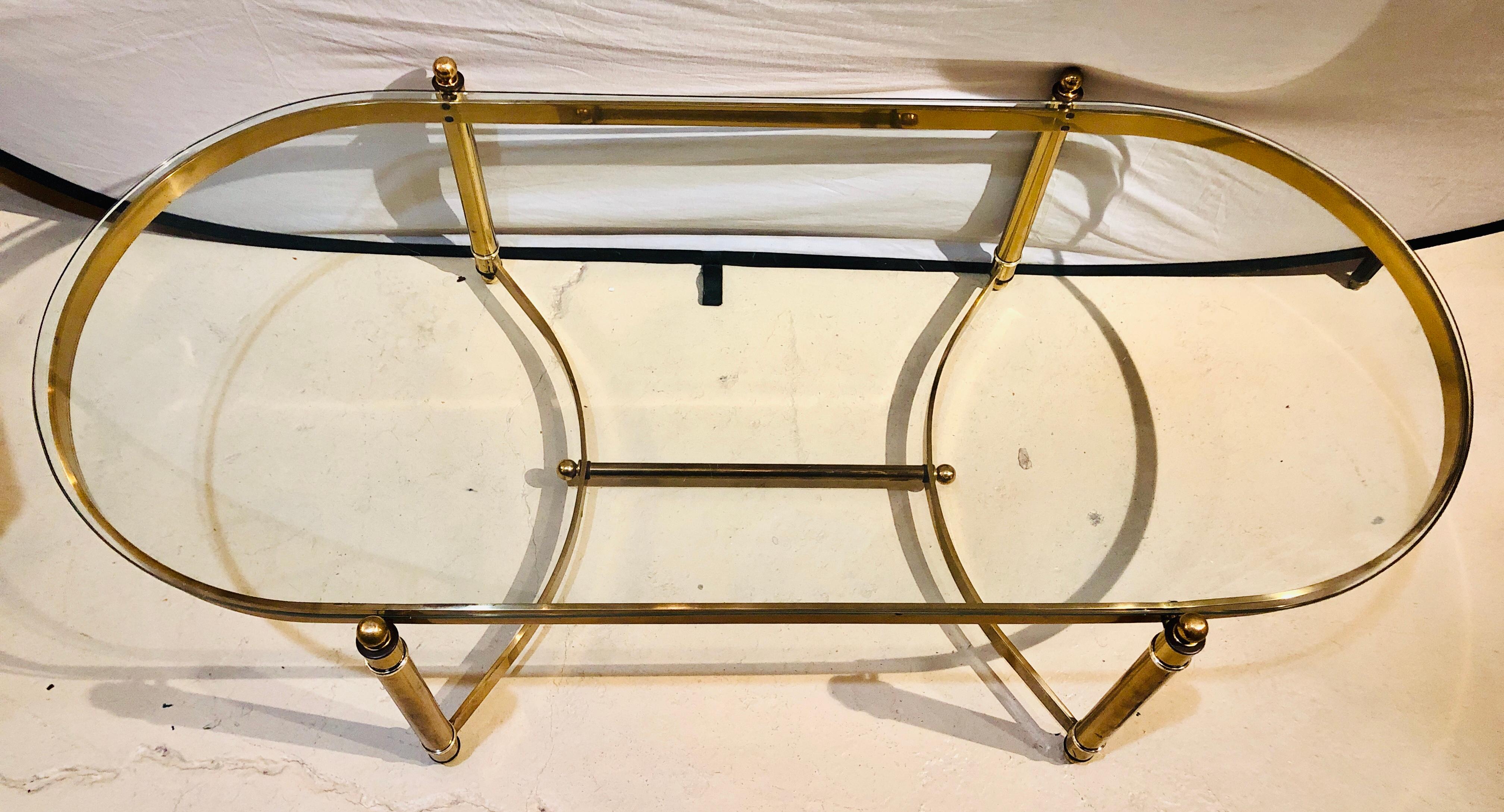 A Hollywood Regency style heavy brass oval coffee table with a glass top. This fine custom quality bass coffee table is large and impressive. The sleek and clean lines are stylish with the legs connecting via a double C-shaped undercarriage