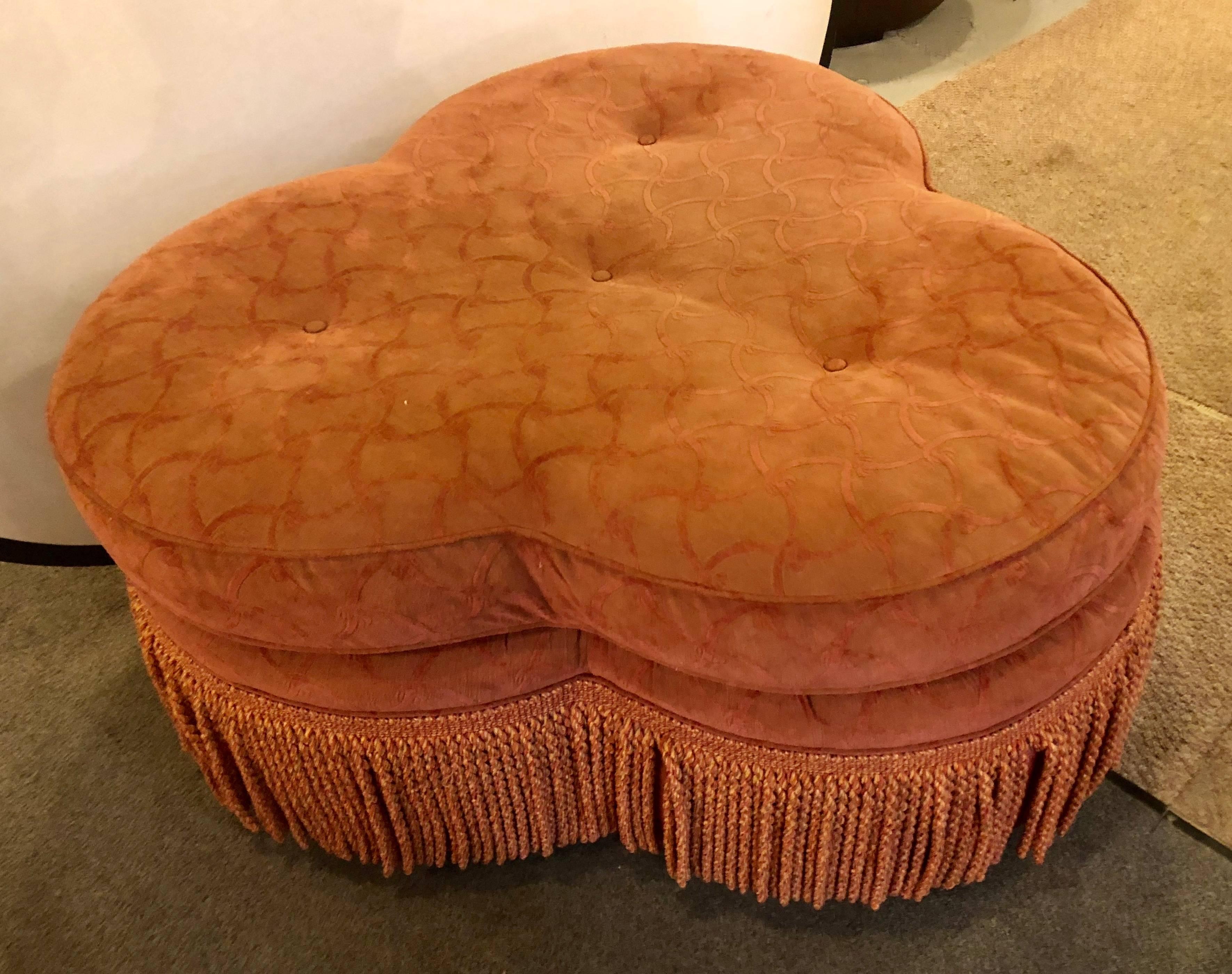 A Hollywood Regency style large clover shaped tufted ottoman or stool. This bright custom quality pouf is very decorative and can be used in multiple areas of the home. Having a tufted sitting area and fringed base this fine ottoman is certain to be