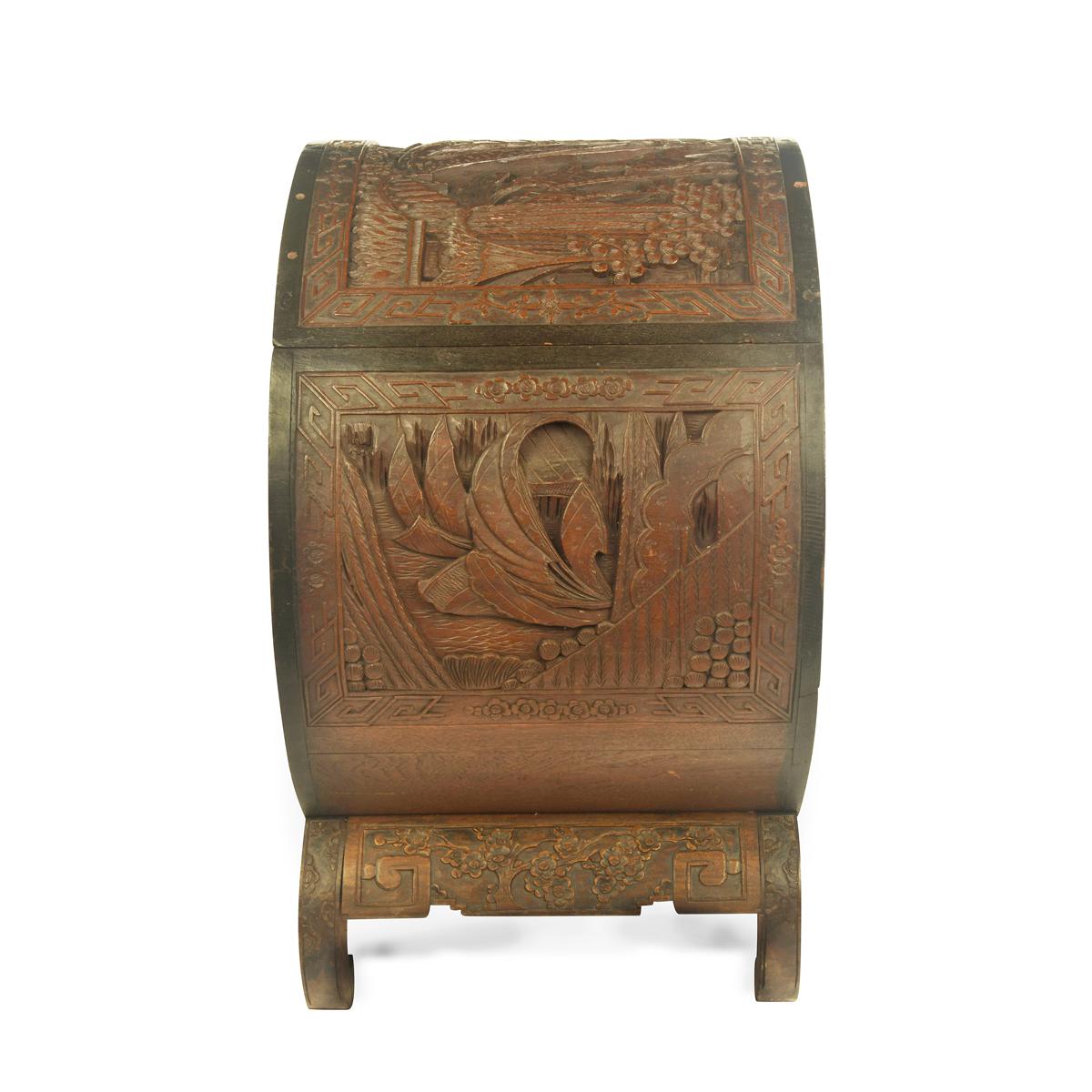 A Hong Kong camphorwood cylindrical chest, the drum shaped body with a hinged lid set on its side on a typical base with short, in-curved legs, incised throughout in high relief with scenes of sailing ships, at sea and by a bridge, and a troop of