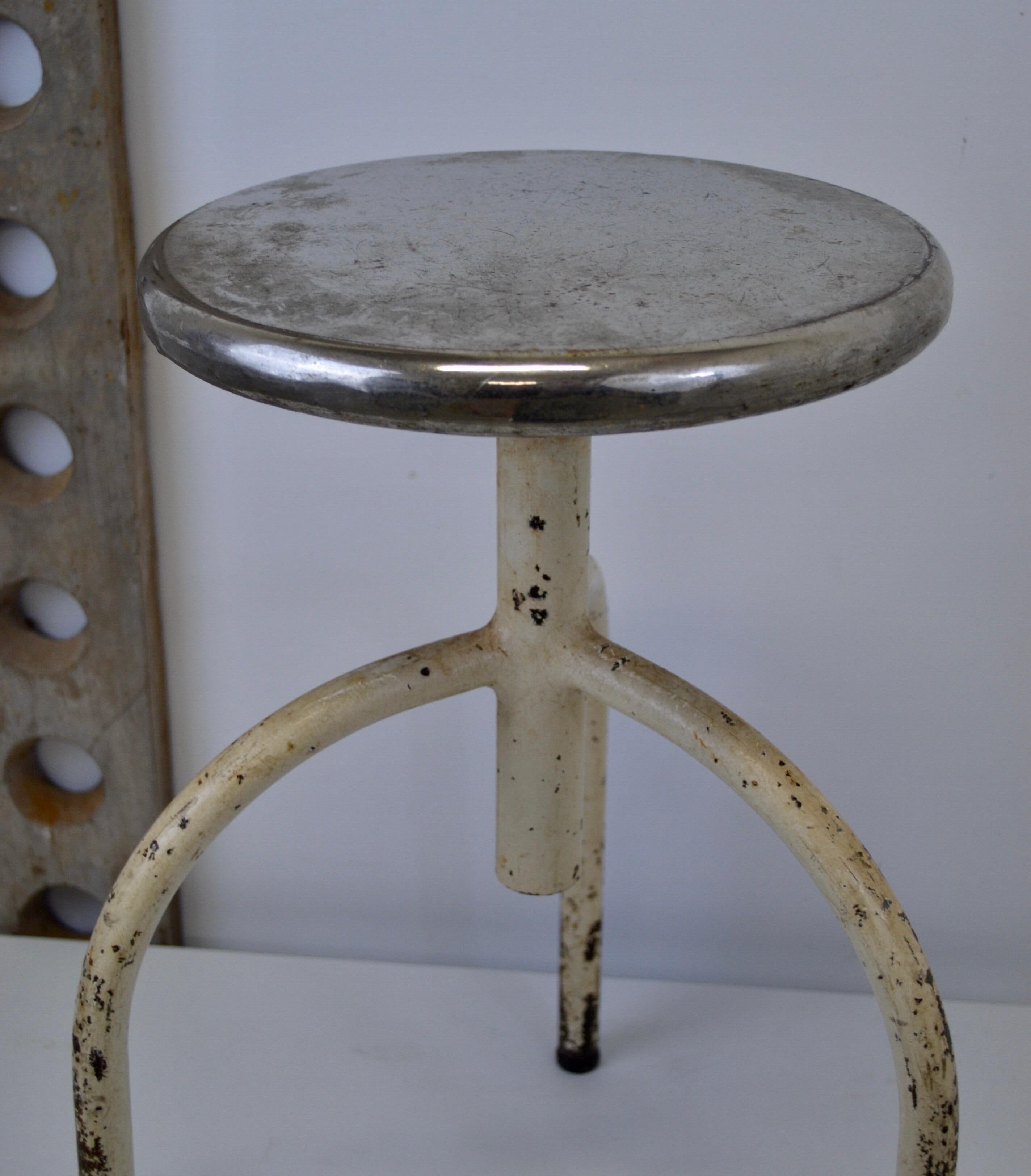 A Hospital dispensary stool c. 1930. Curved steel and sheet metal, adjustment by endless screw. 
Very stable and solid. 
Superb period patina.
Dimensions: H45/70 D30 [cm]
