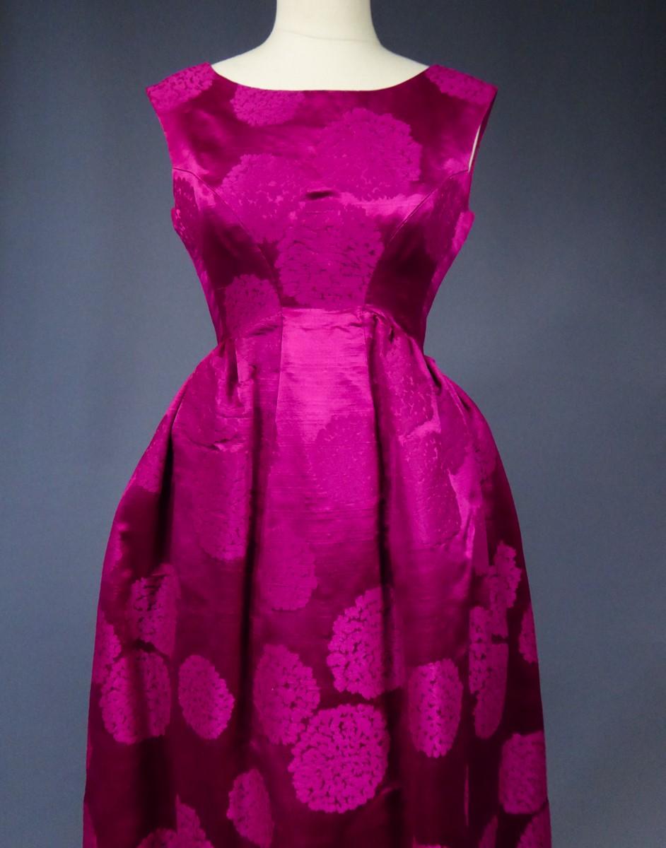 Collection 1960
France

A damask gazar silk long evening gown with large fuschia hydrangea flowers balls. High-waisted bodice with flared back and little train, oblique effect, sleeveless and boat-neckline. Petticoat puffed under the hips giving