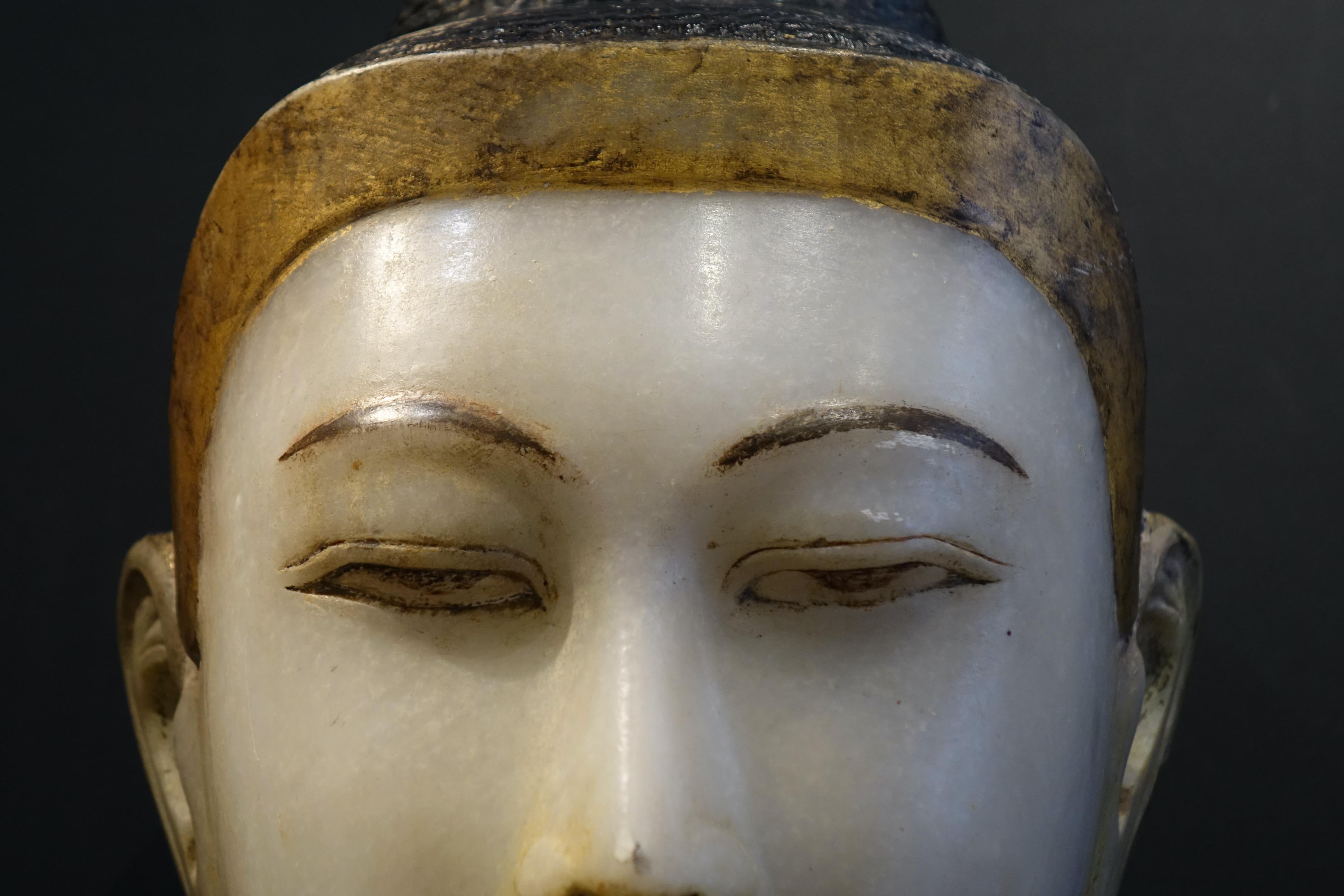 Grande testa (altezza 40) di Buddha in marmo con tracce di policromia, occhi semichiusi, sormontata dalla protuberanza cranica di Usnisha, dipinta in lacca nera (usura). 
La base dell'acconciatura riccia è evidenziata con una foglia d'oro. 
Lobi