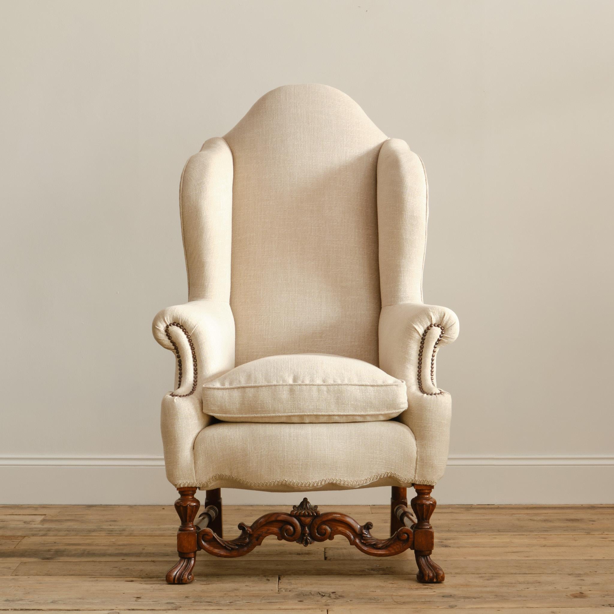 A huge country house 19th century wingback armchair in the William & Mary taste. Raised on crisply carved oak legs with stretchers. The beige linen upholstery in recent and very much ready for use. 

57cm seat height