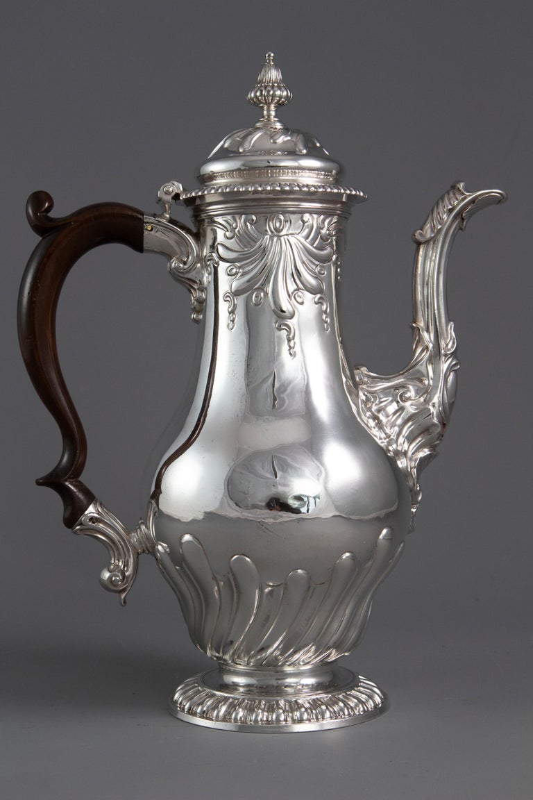 An important George II silver coffee pot by Samuel Courtauld, London 1757. Of raised baluster form, embossed scroll and fluted decoration, cast leaf capped spout, the hinged cover with a fluted acorn finial, and gadroon border, on a raised circular