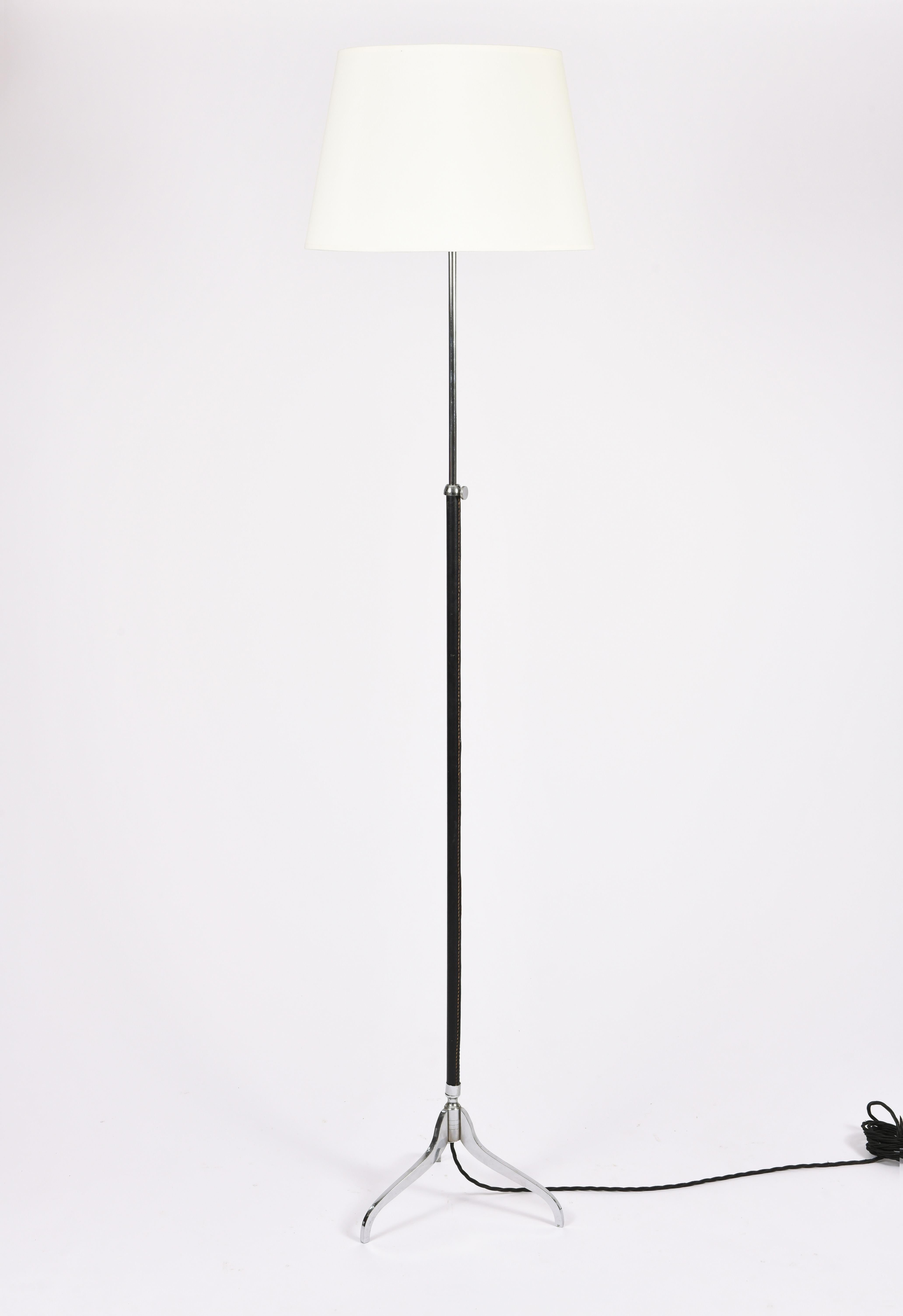 A saddle stitched black leather and nickel plated brass tripod floor lamp, in the manner of Jacques Adnet,
with a telescopic stem and a bespoke ivory fabric tapered shade 
France, circa 1950
